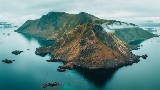 Aerial view of a mountainous island surrounded by misty waters and small rocky outcrops.