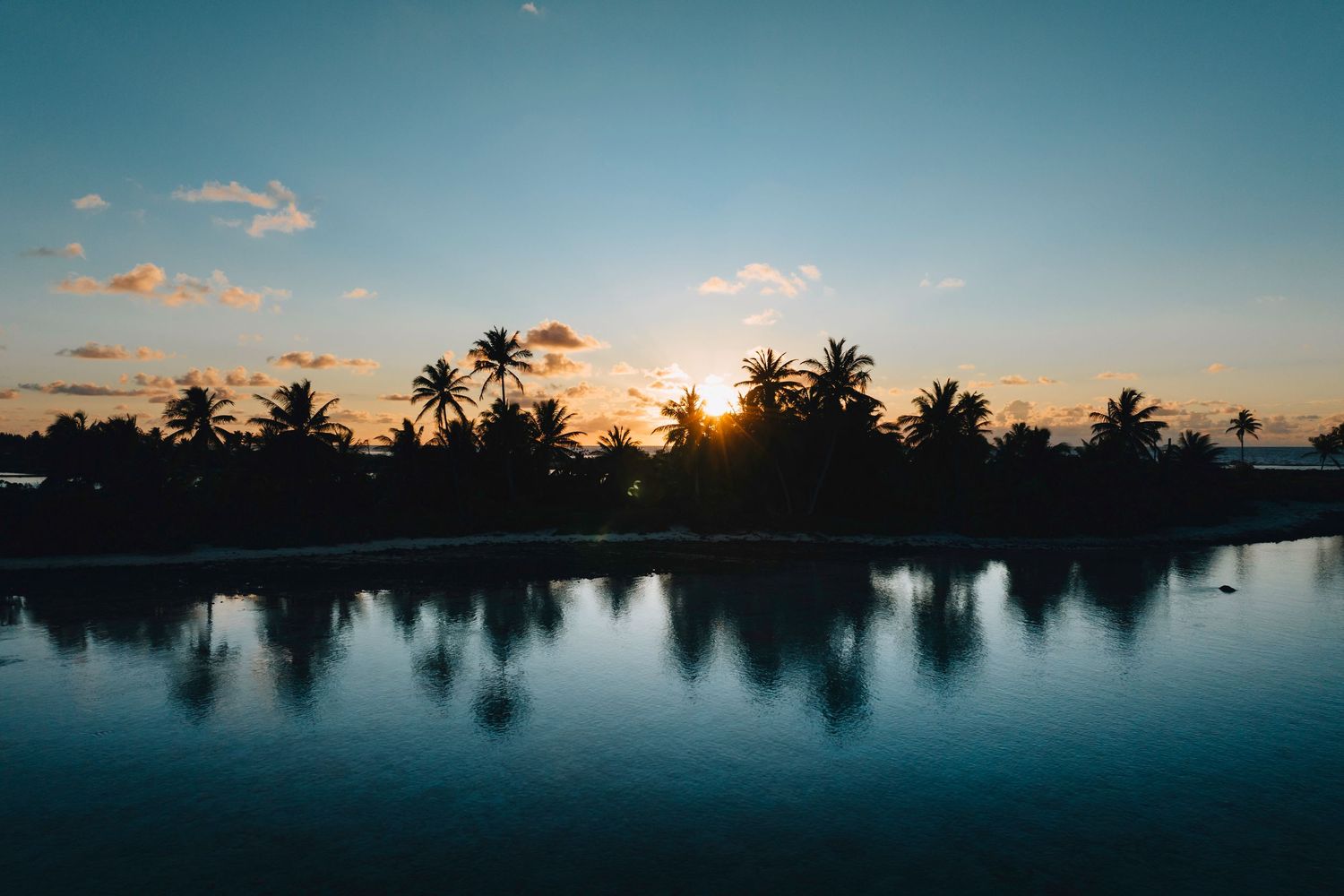 Silhouette of palm trees reflected in calm waters during a tropical sunset.