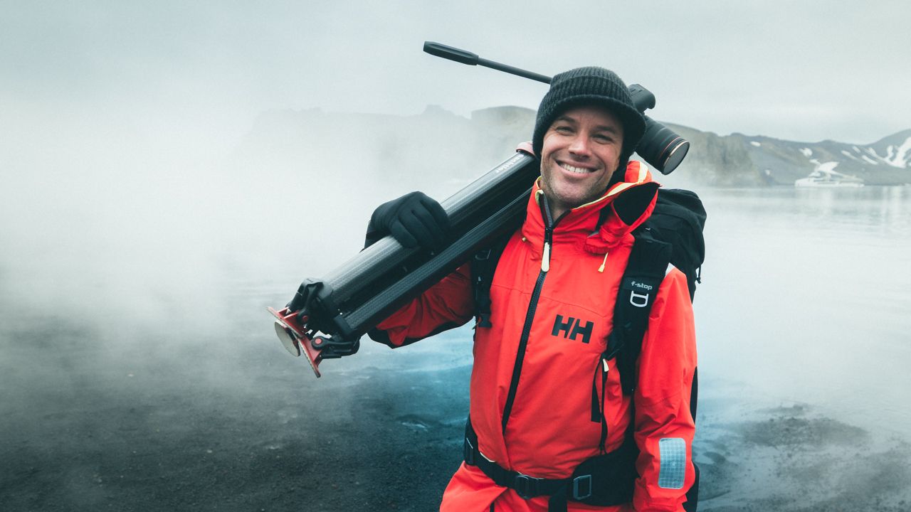 Person in red winter gear carrying camera equipment in foggy mountainous landscape.