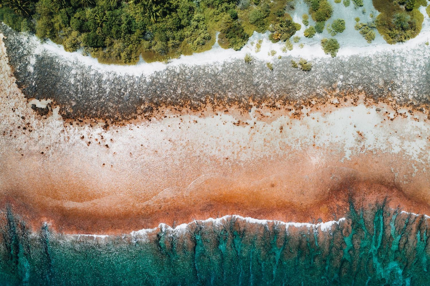 Abstract aerial view of a coastline with crashing waves creating patterns between turquoise water and beach.
