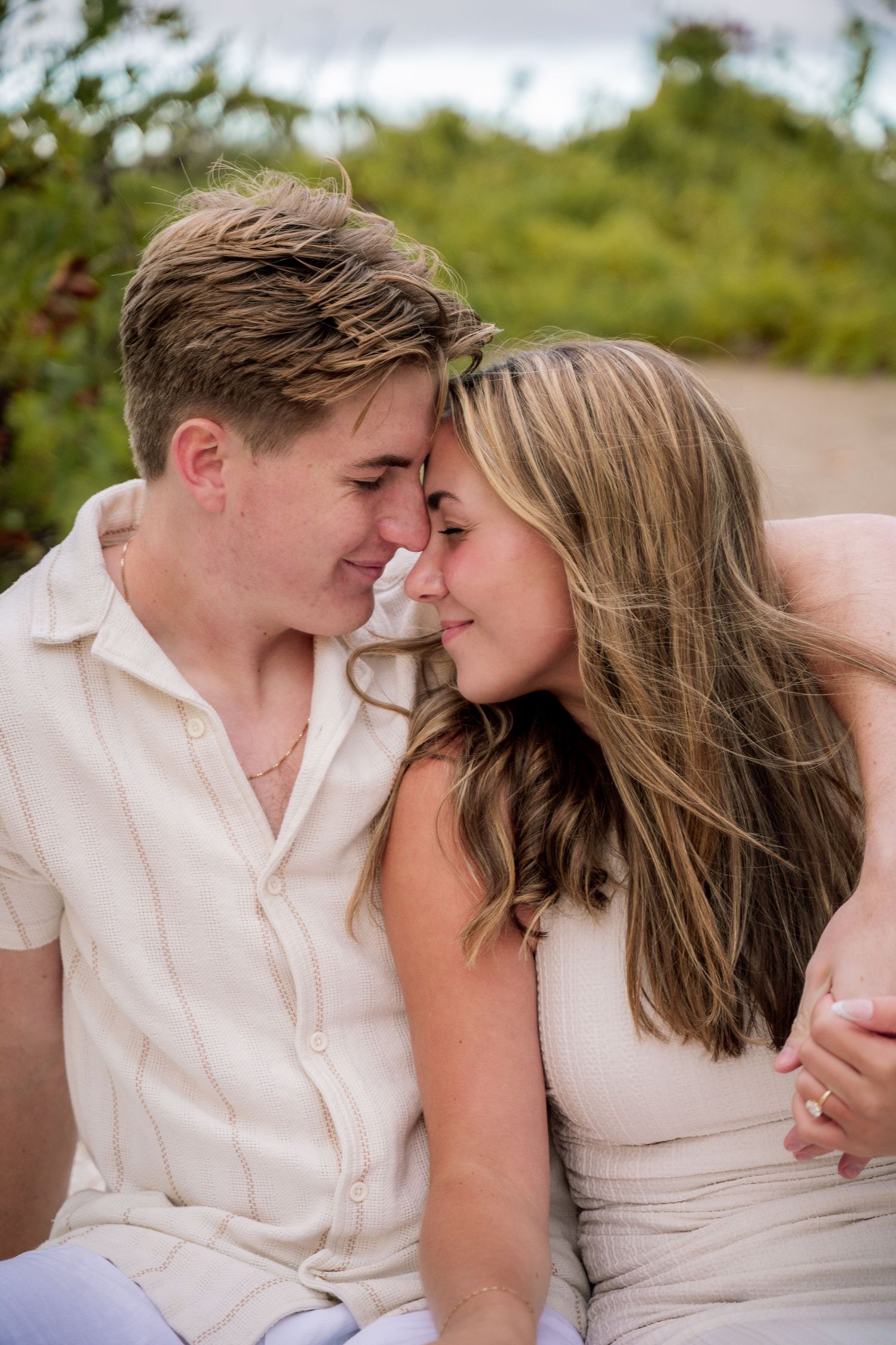 A romantic couple shares an intimate moment touching foreheads while sitting outdoors on a sunny day.