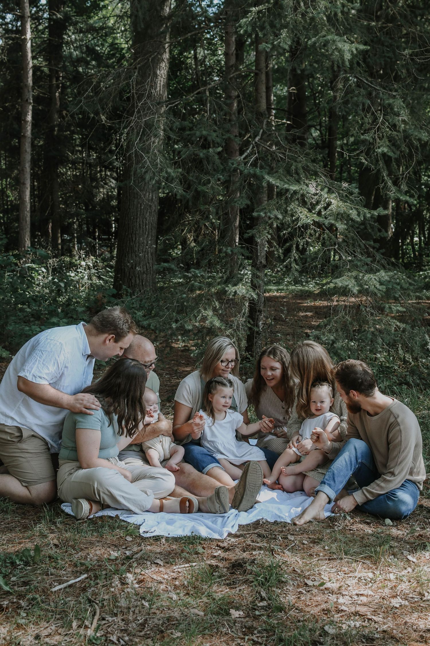 Family laying together on forest floor in matching white outfits during outdoor photo session.