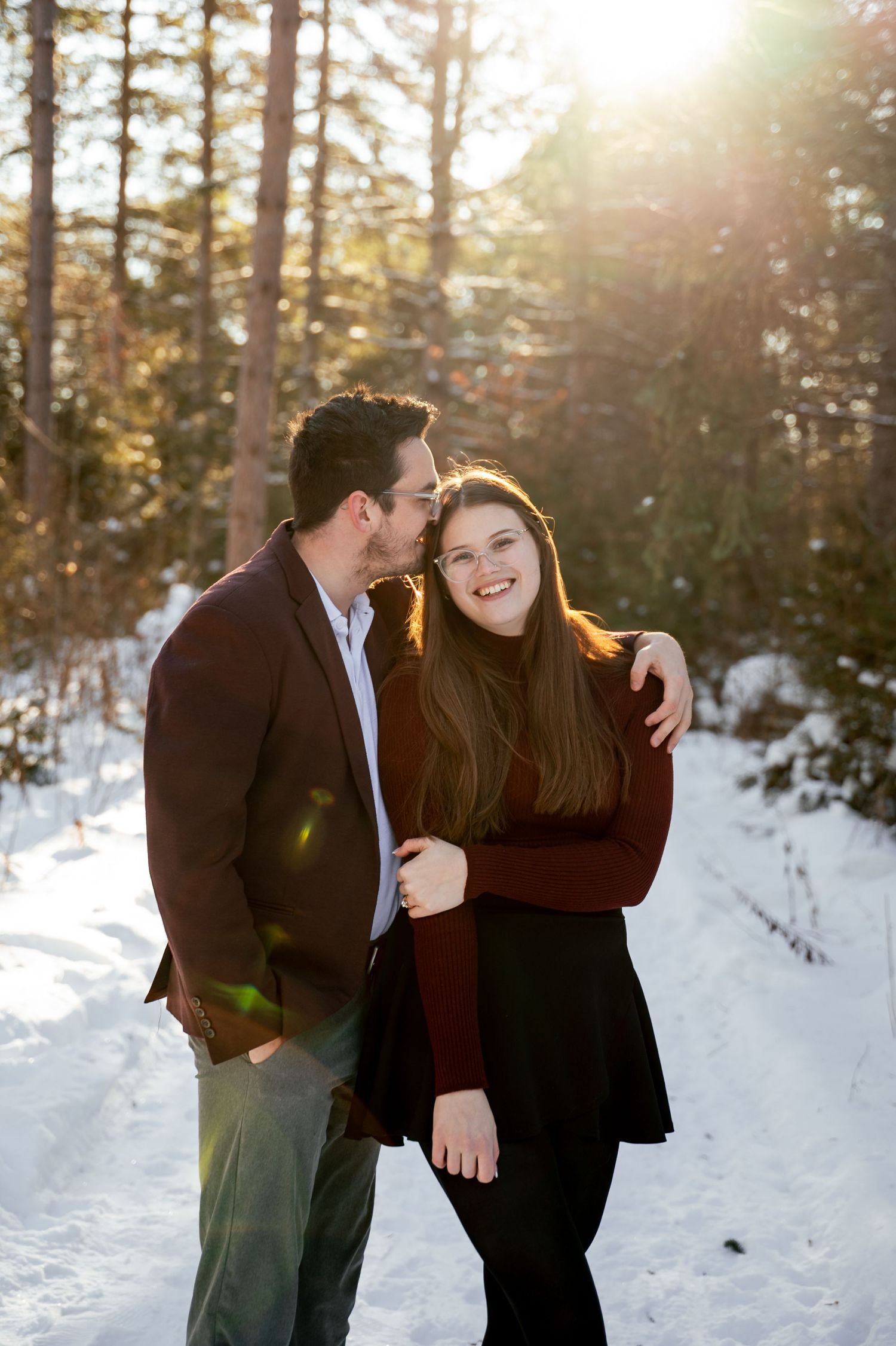 Couple shares romantic moments in a snowy winter forest setting during golden hour sunset.