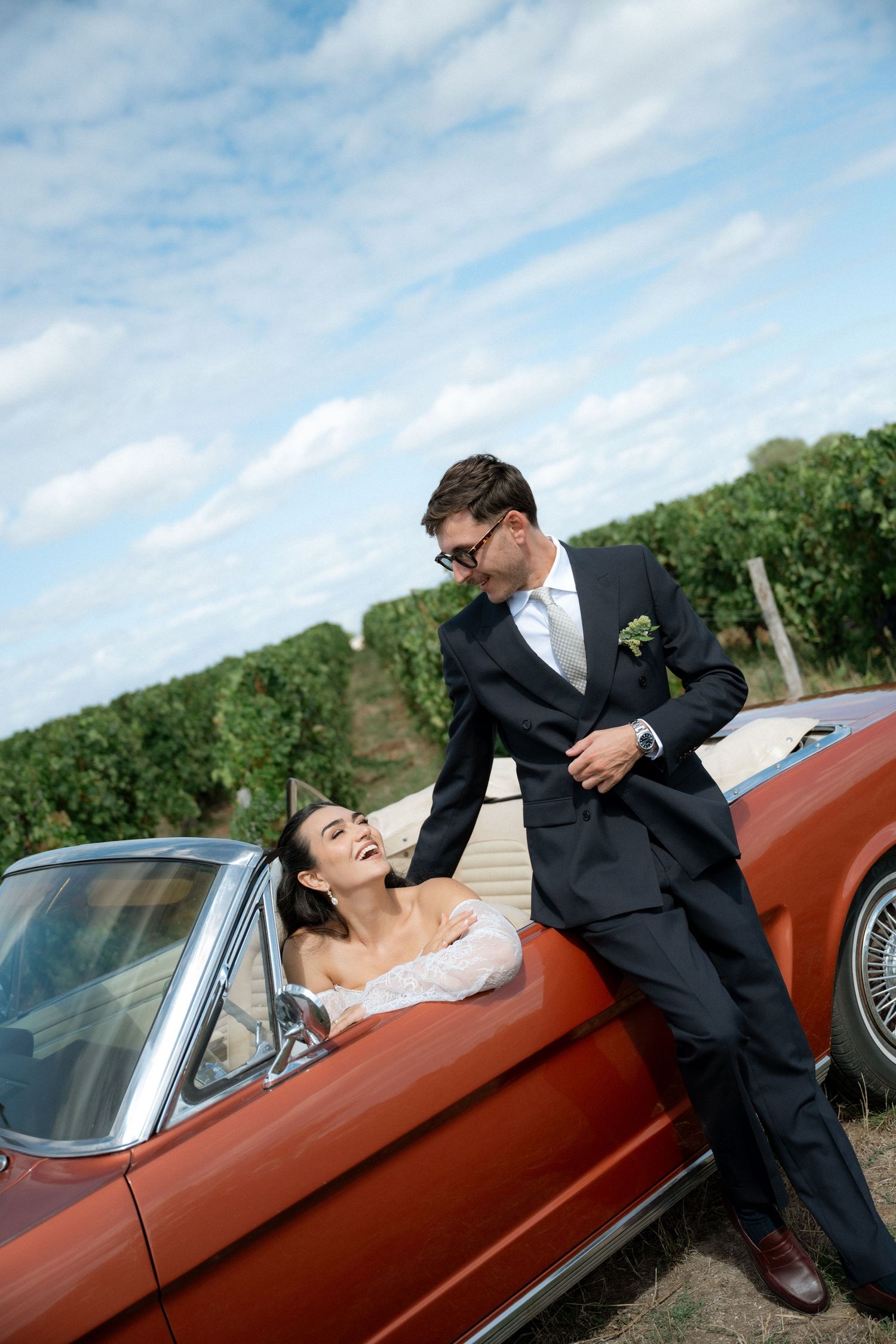 Wedding couple poses playfully with vintage red car in a series of romantic outdoor shots.