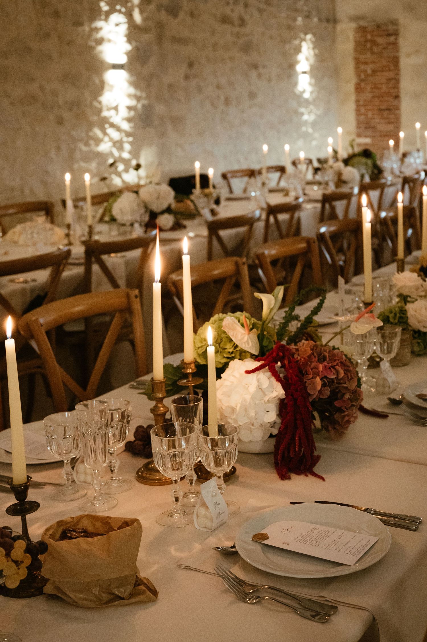 Elegant wedding reception table setting with glowing candles and floral arrangements in a rustic stone venue.