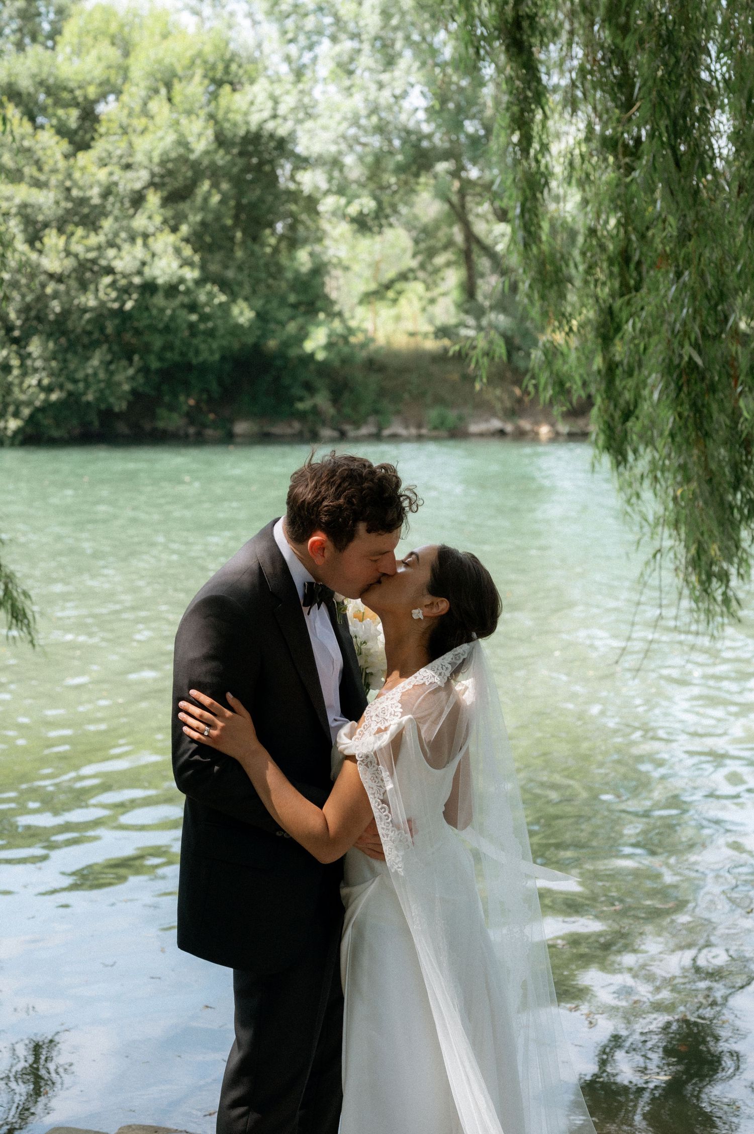 Romantic wedding portraits by a lake with weeping willow trees creating a dreamy backdrop.