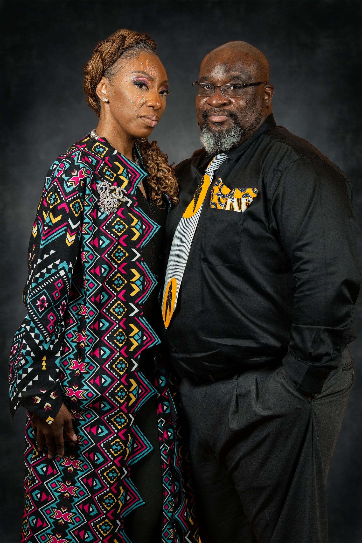 Man and woman pose together in coordinating African-inspired formal attire for portrait.