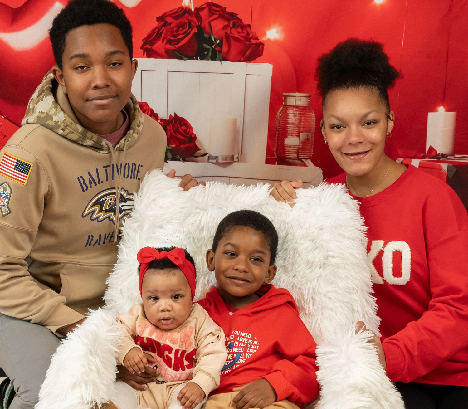 Family of four posing for a Valentine's Day photo with red roses and festive decorations in the background.