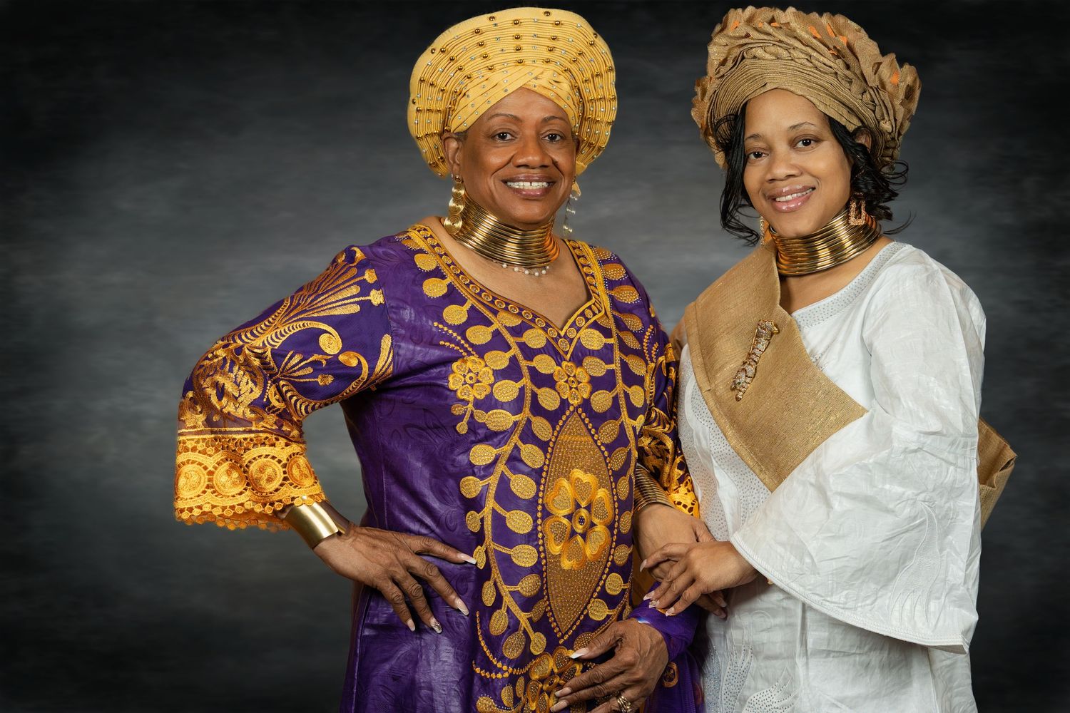 Two women in stunning gold and purple African traditional dress and headwraps pose.