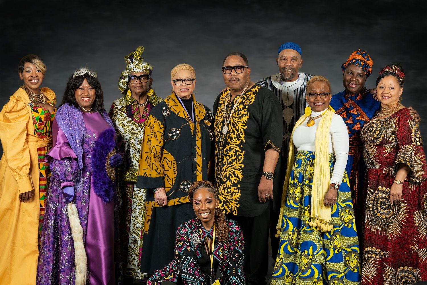 Group of ten people in colorful African traditional clothing pose for a group photo.