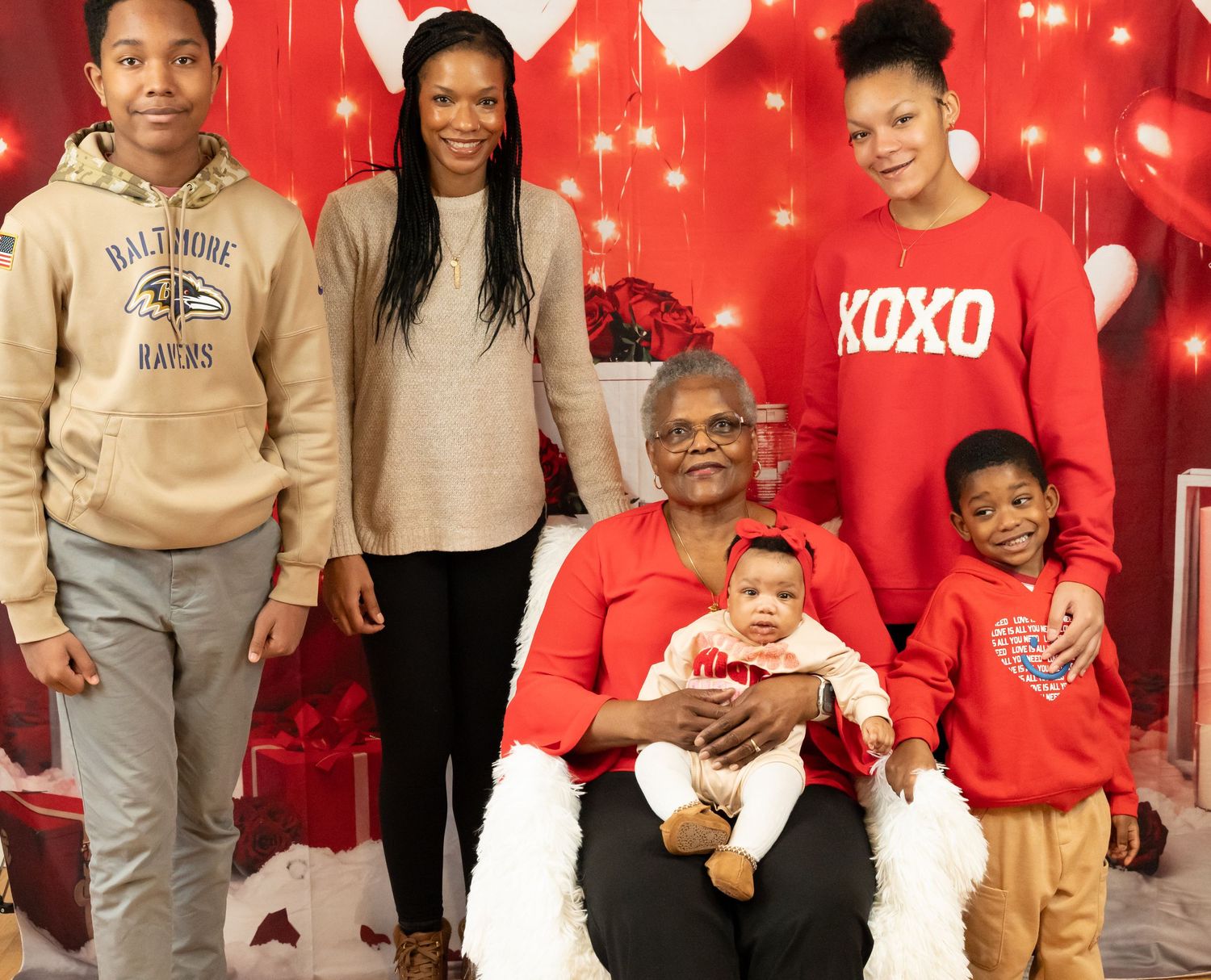 Family portrait with five generations posing together for a Valentine's Day themed photo with red decorations.