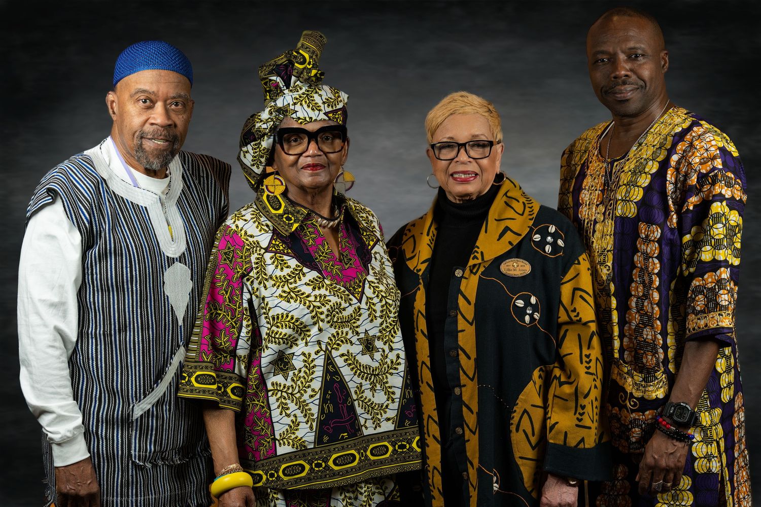 Two couples pose together wearing traditional African cultural attire in rich colors.