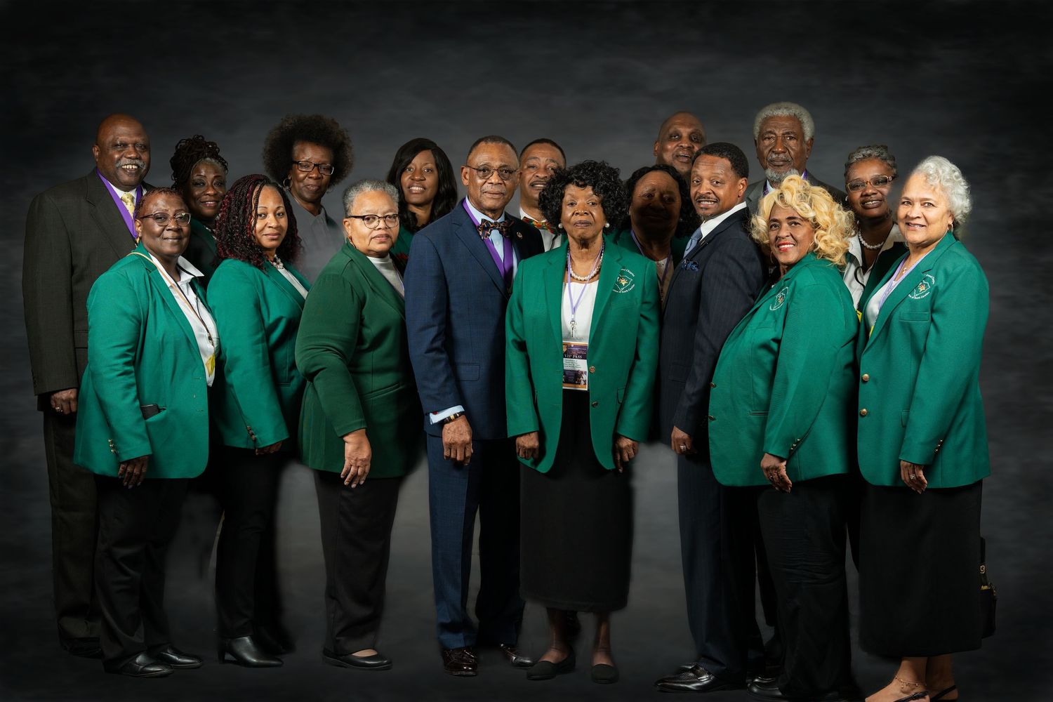 A large group of people wearing matching green blazers pose together for a formal group portrait.