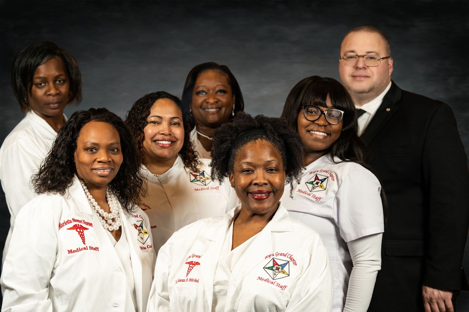 A group of six women in white uniforms and one man in a suit pose together for a group portrait.