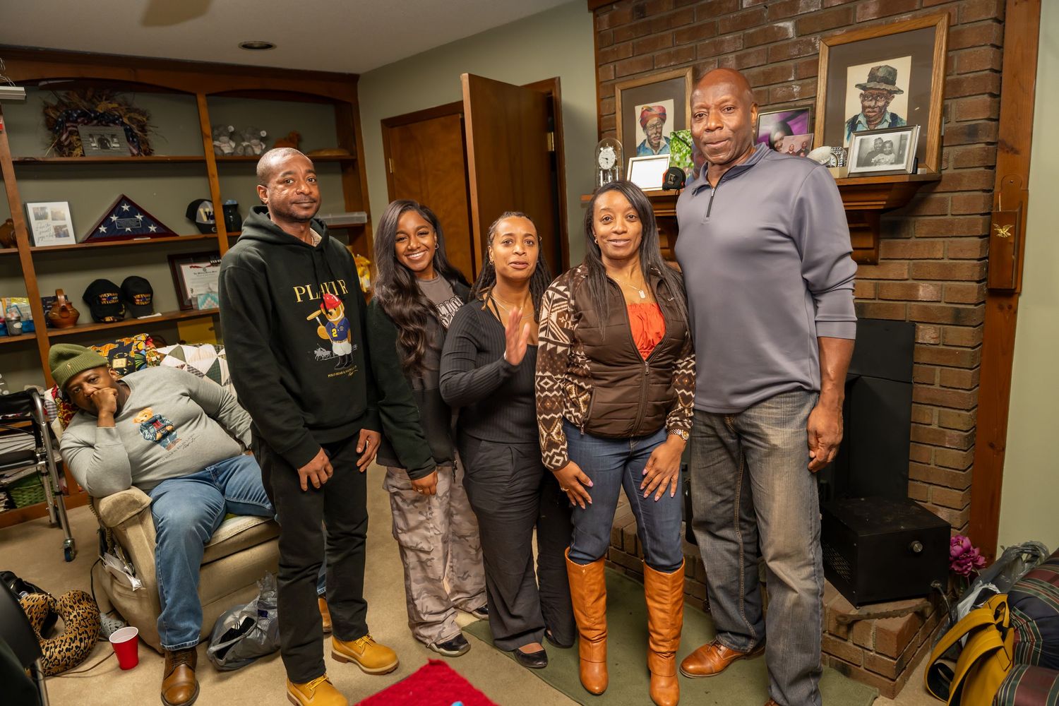 Five people posing together indoors in a cozy room with bookshelves and framed photos on the wall.