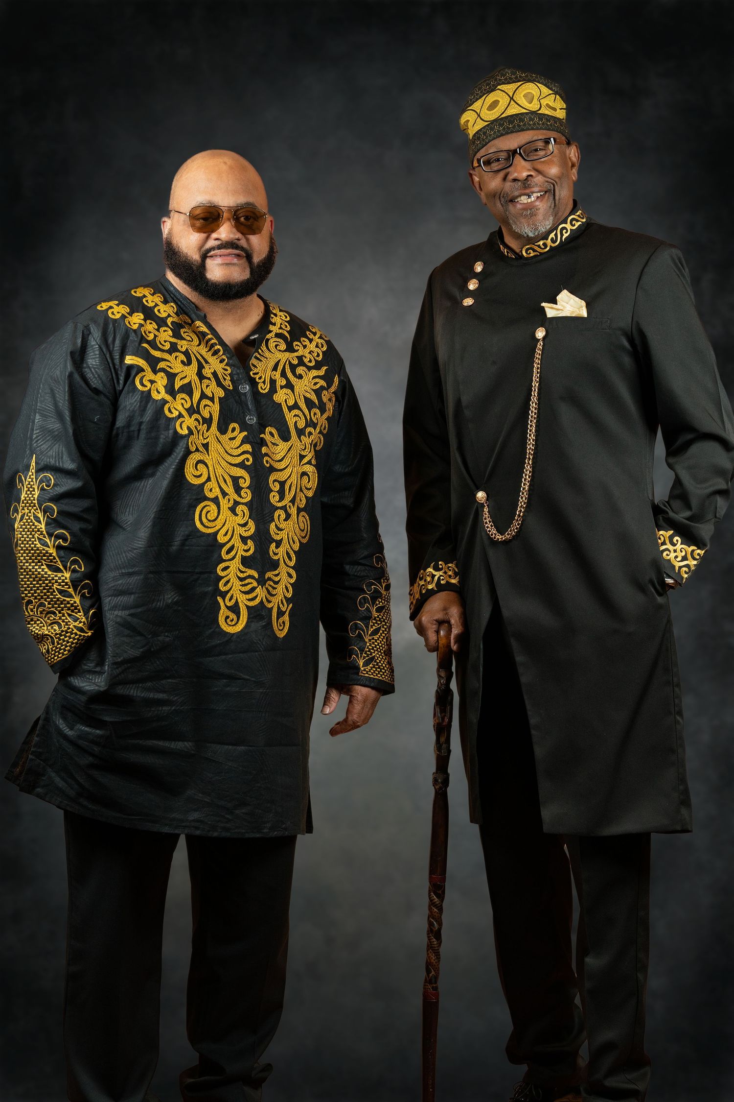 Two men in elegant black and gold African attire pose for a formal portrait.