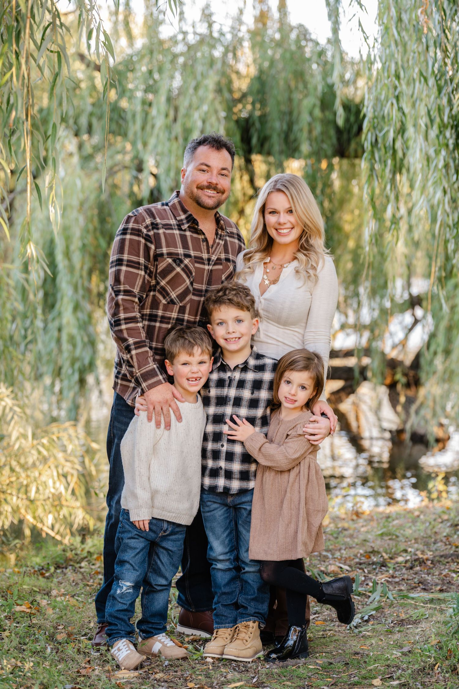 family posing and smiling under pretty willow tree