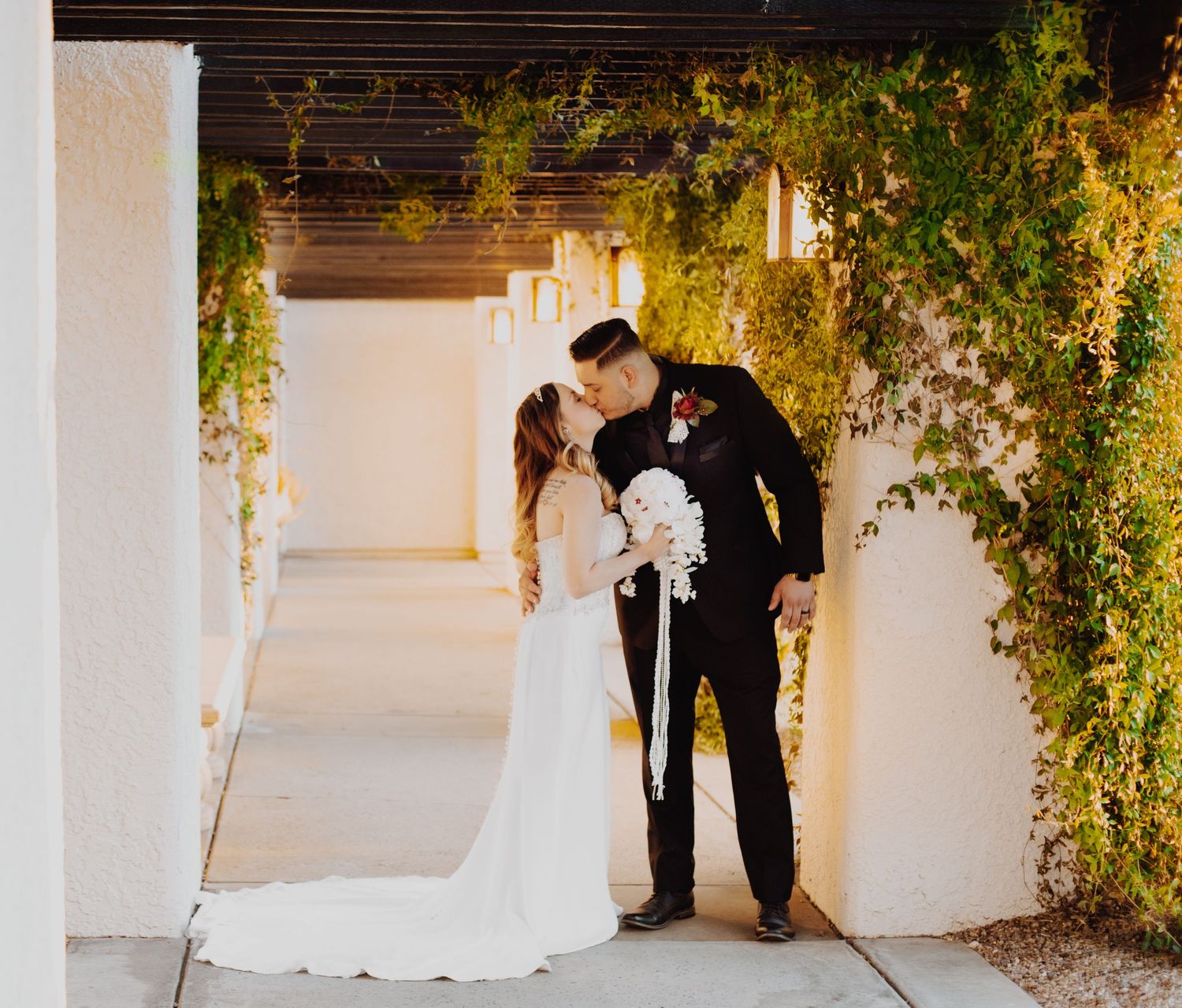 Wedding couple shares intimate moment under archway decorated with hanging greenery.