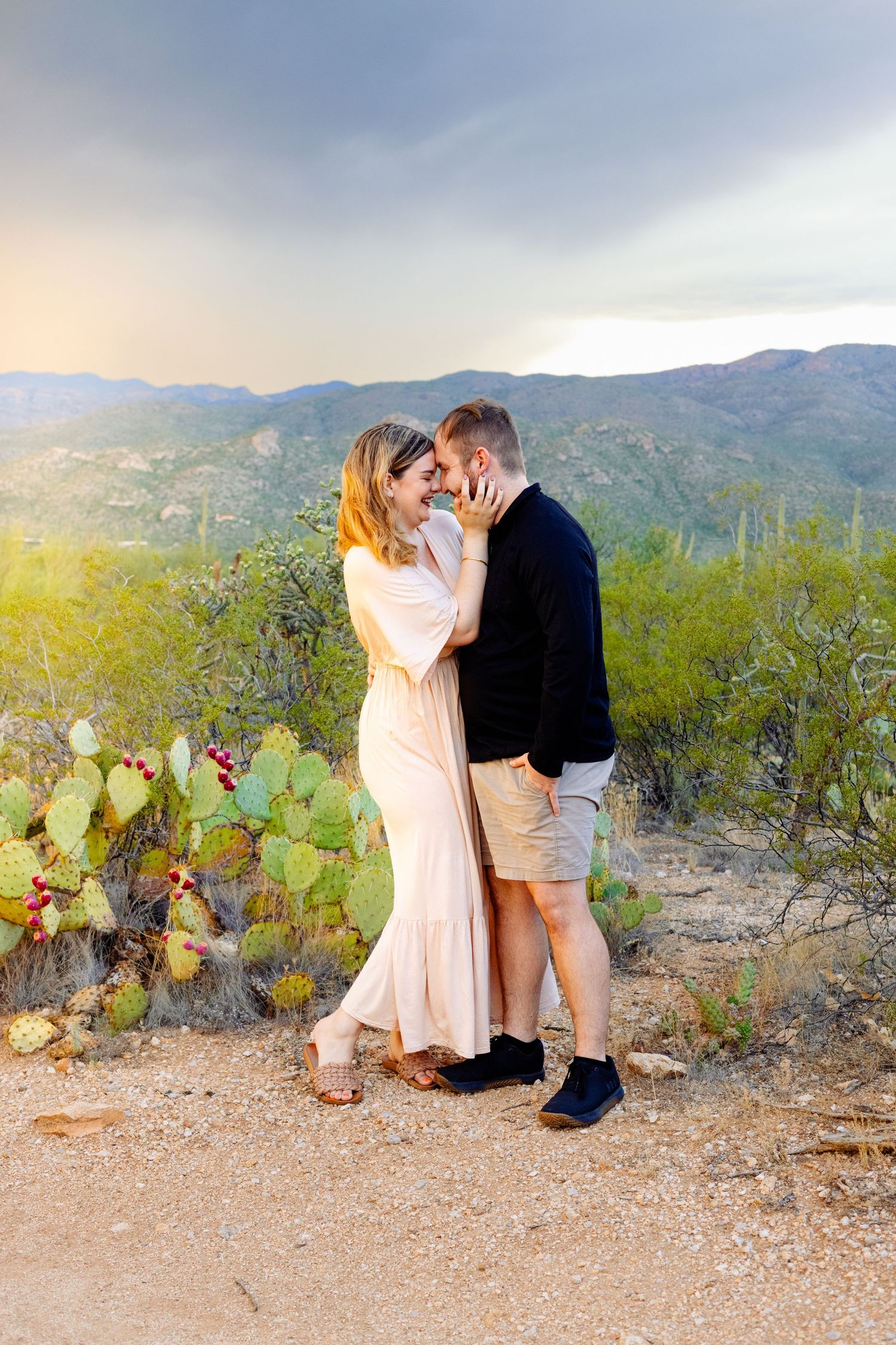Romantic desert engagement photo with mountains and cacti during golden hour.