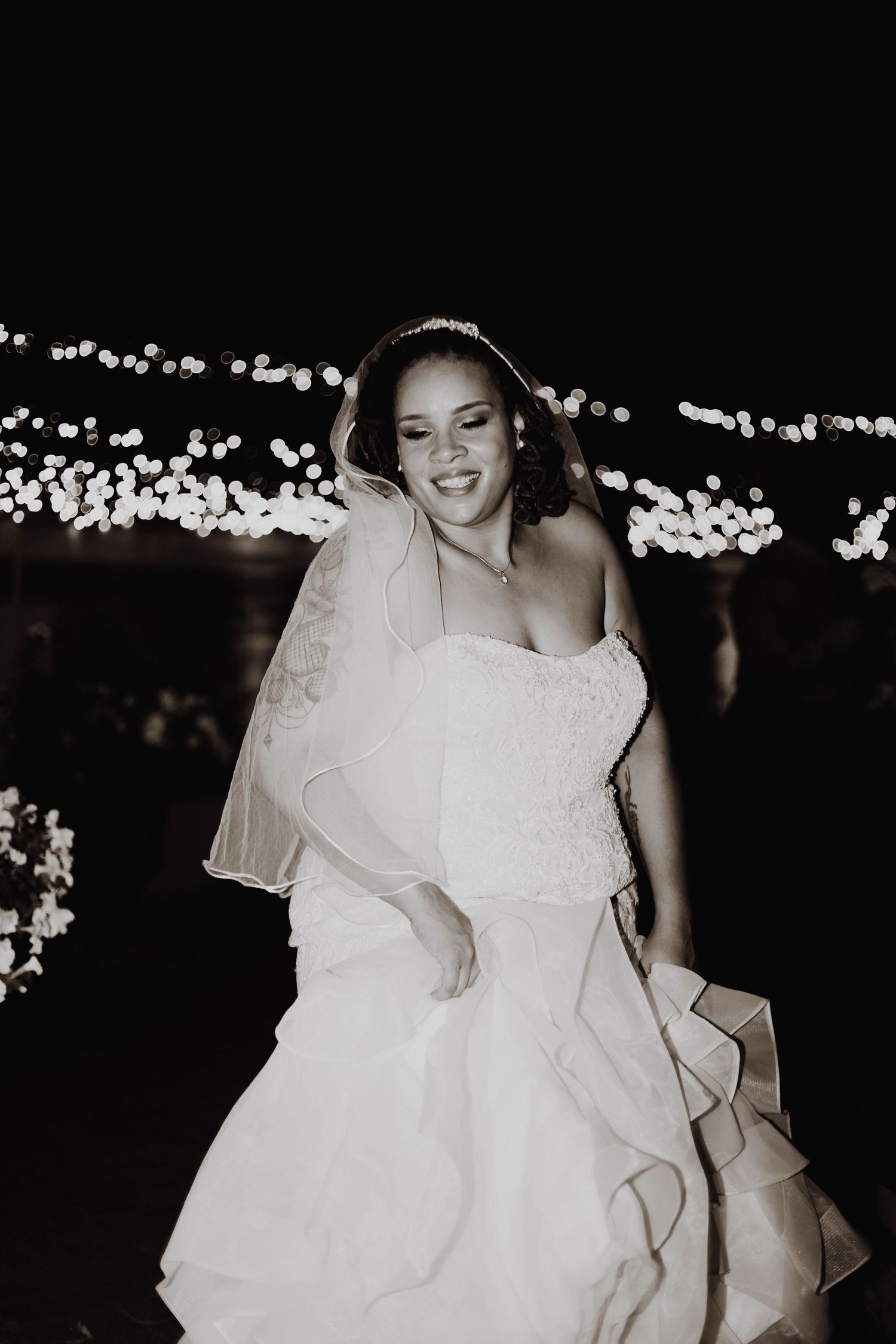 A bride in a white wedding dress dances joyfully under twinkling lights at night.