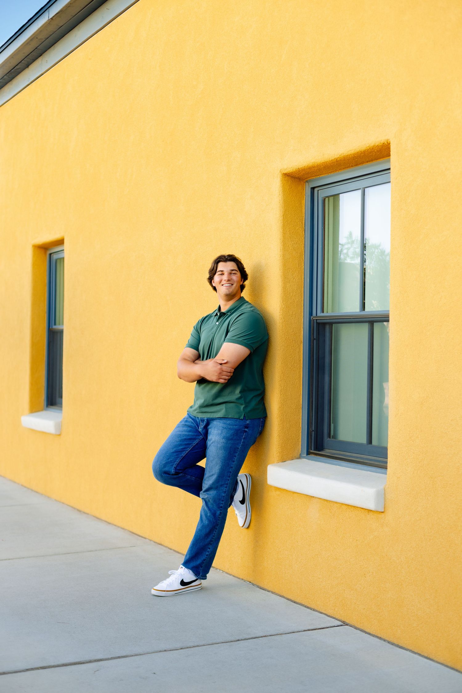 A casual portrait against a vibrant yellow wall with green-trimmed windows.