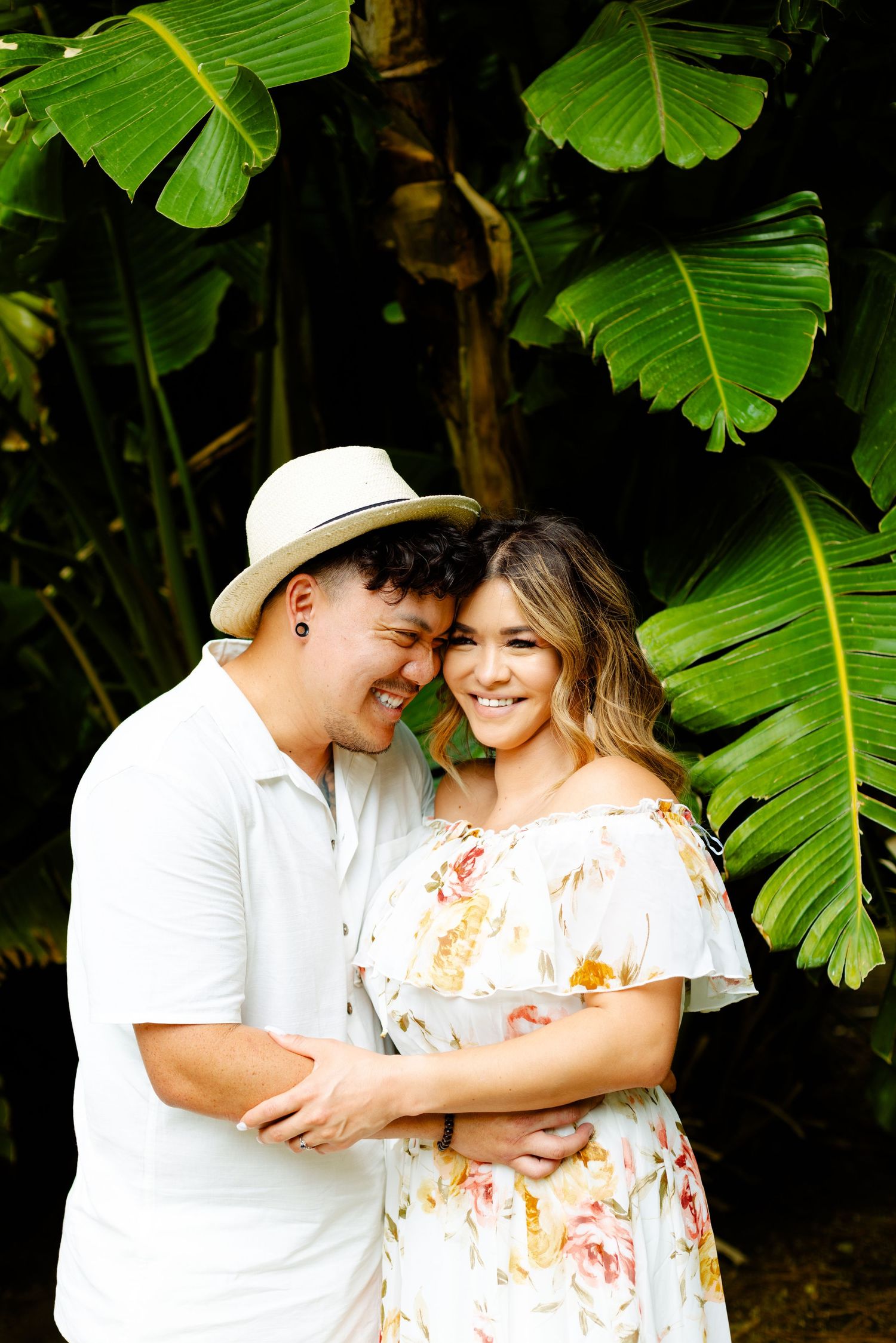 Romantic portrait under large tropical leaves with couple sharing intimate moment.