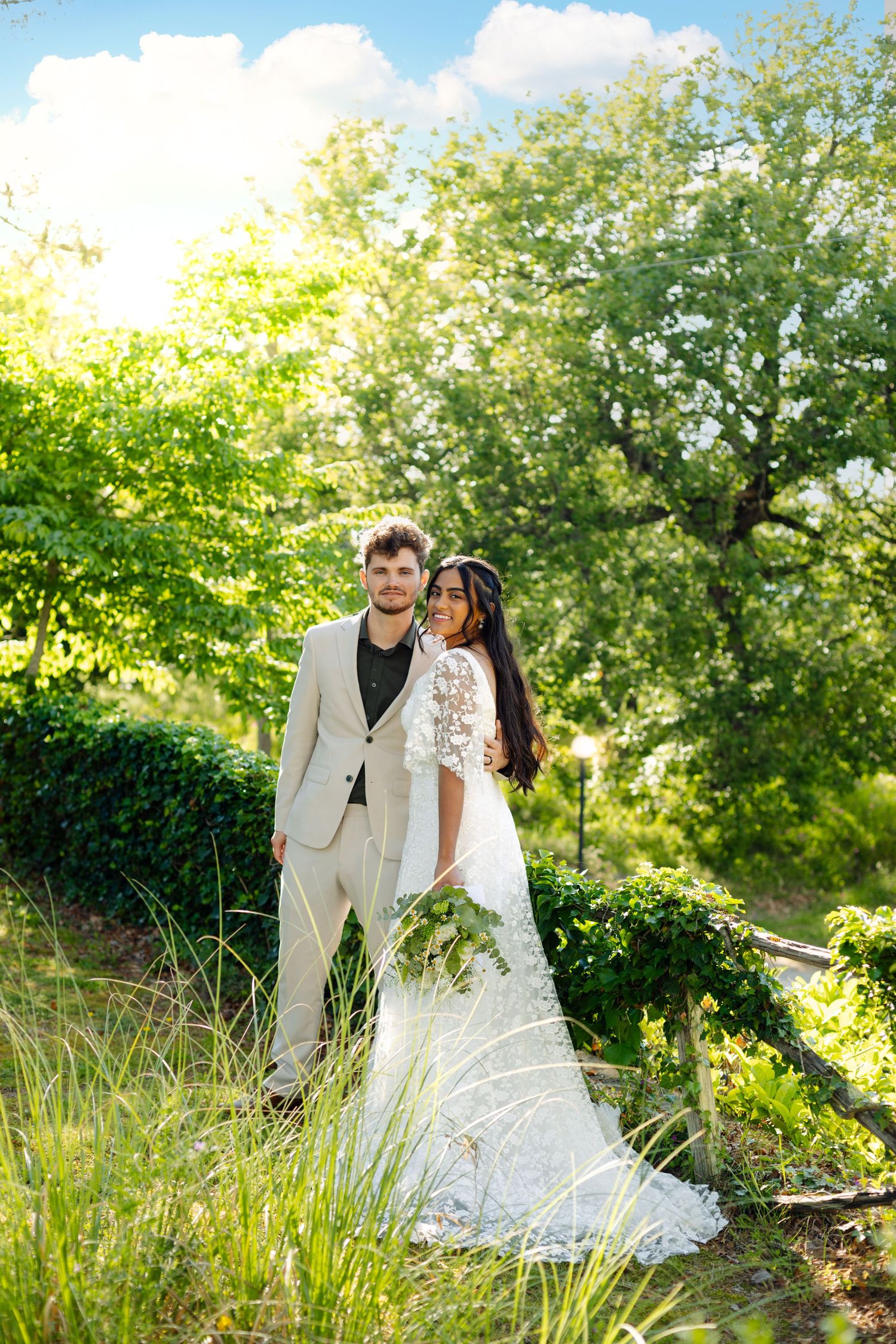 Newlyweds pose together on a grassy hillside in formal wedding attire.