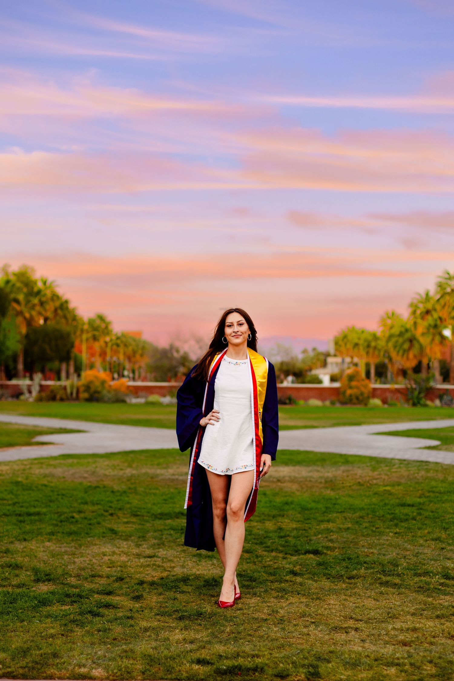 Graduate walks across a grassy field during a colorful sunset.