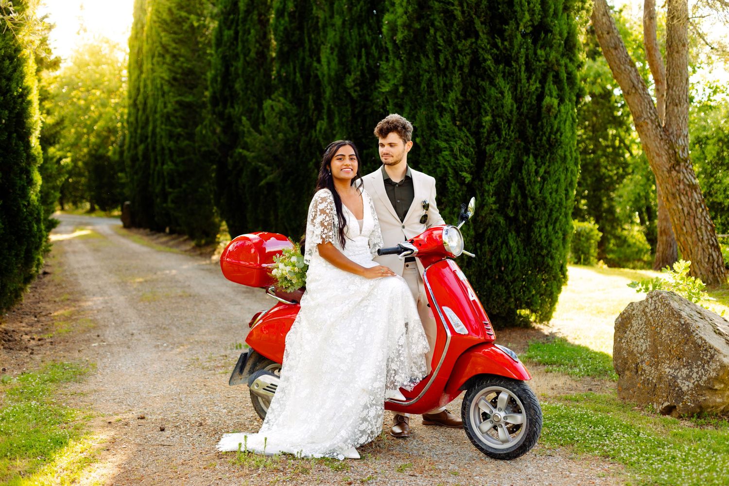 A red Vespa scooter adds vintage charm to outdoor wedding photos.