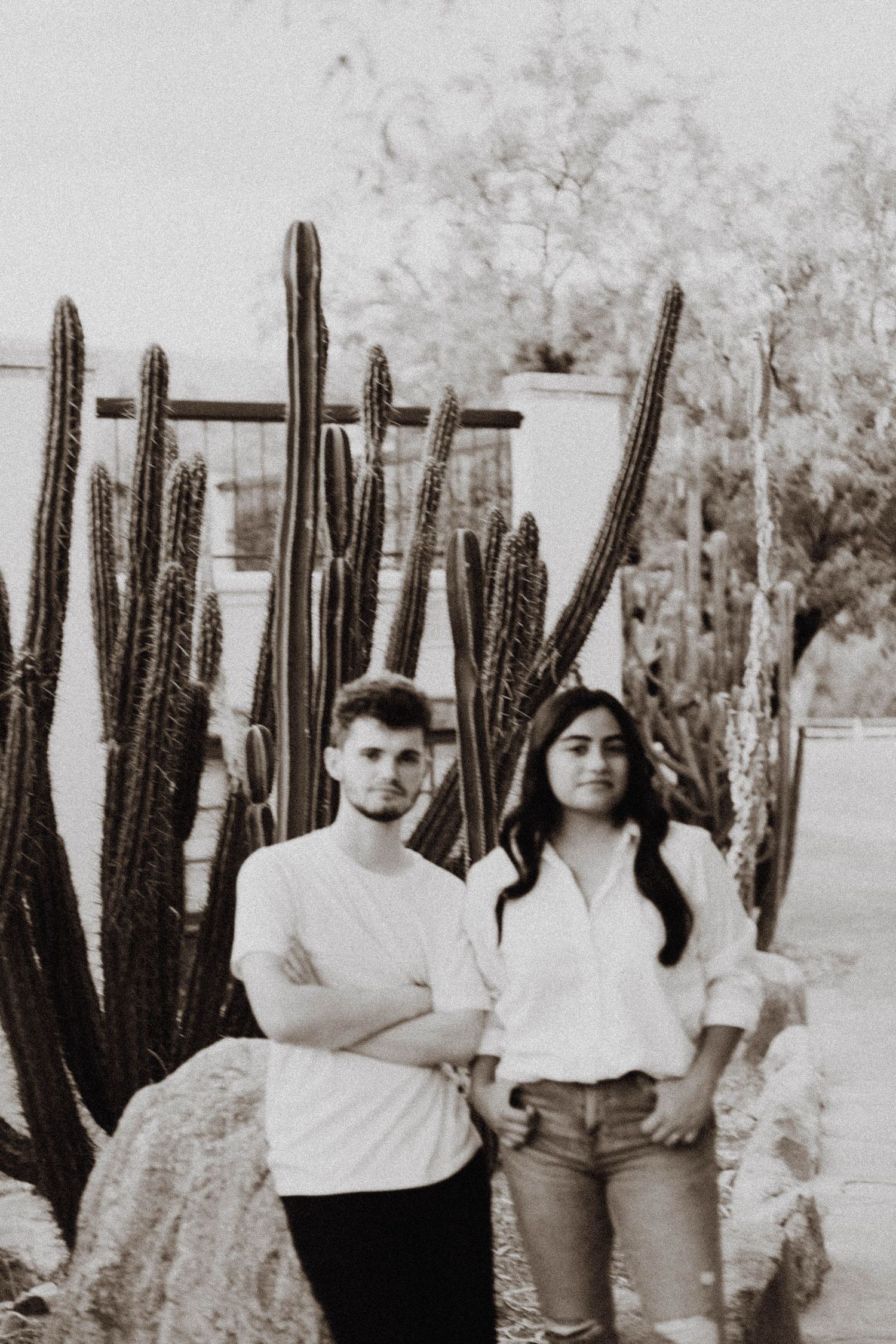 A couple poses in front of tall desert cacti in a black and white photograph.