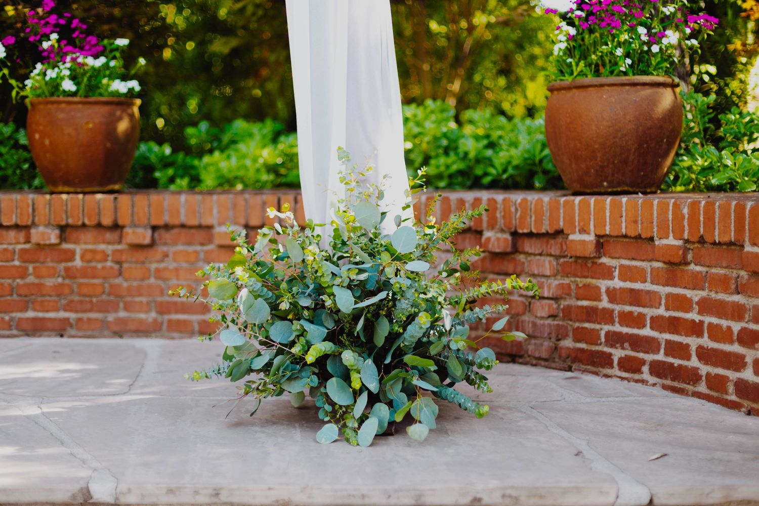 Decorative succulent arrangement at base of white column with brick wall and flowering planters.