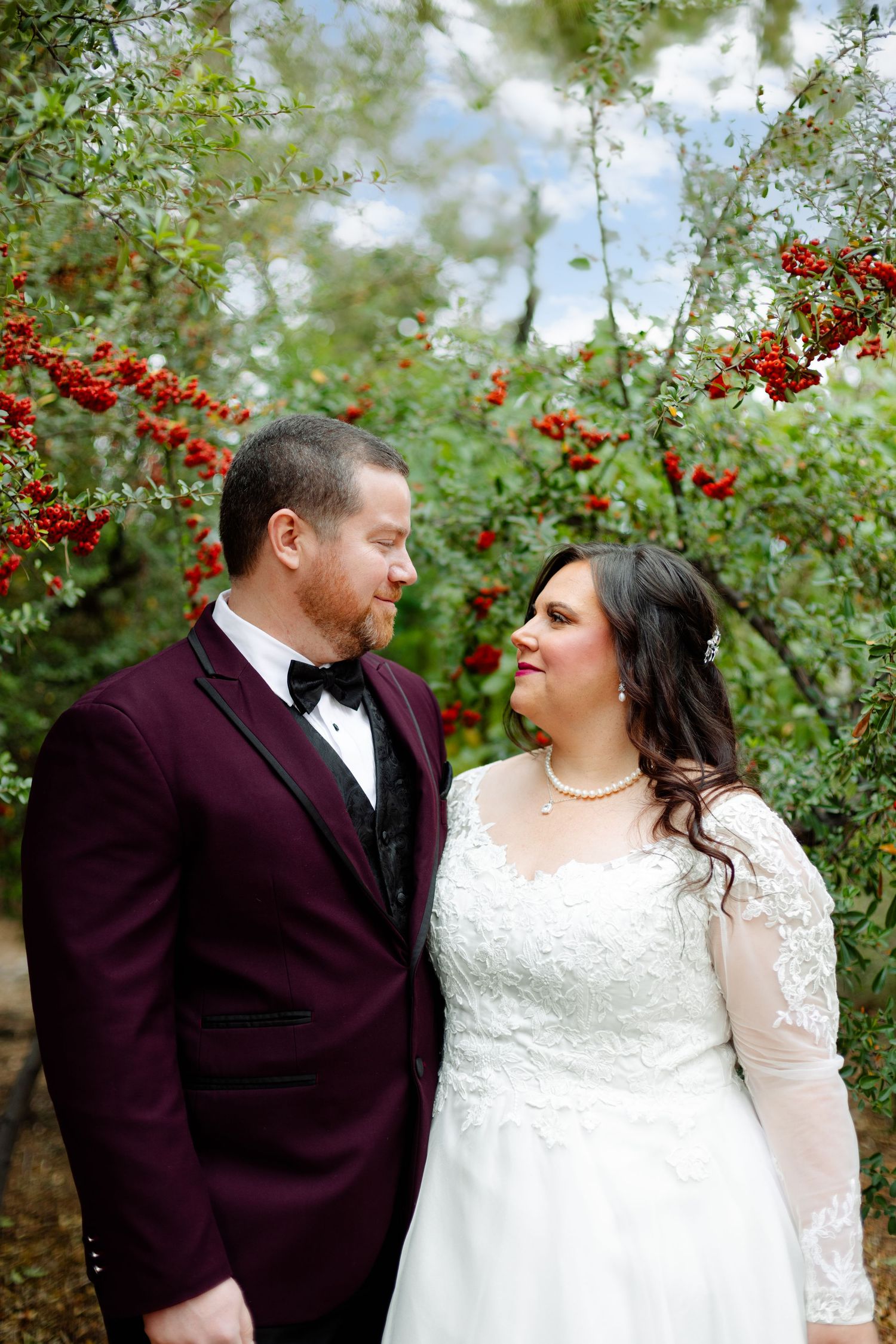 A romantic wedding portrait with red berries and greenery in the background.