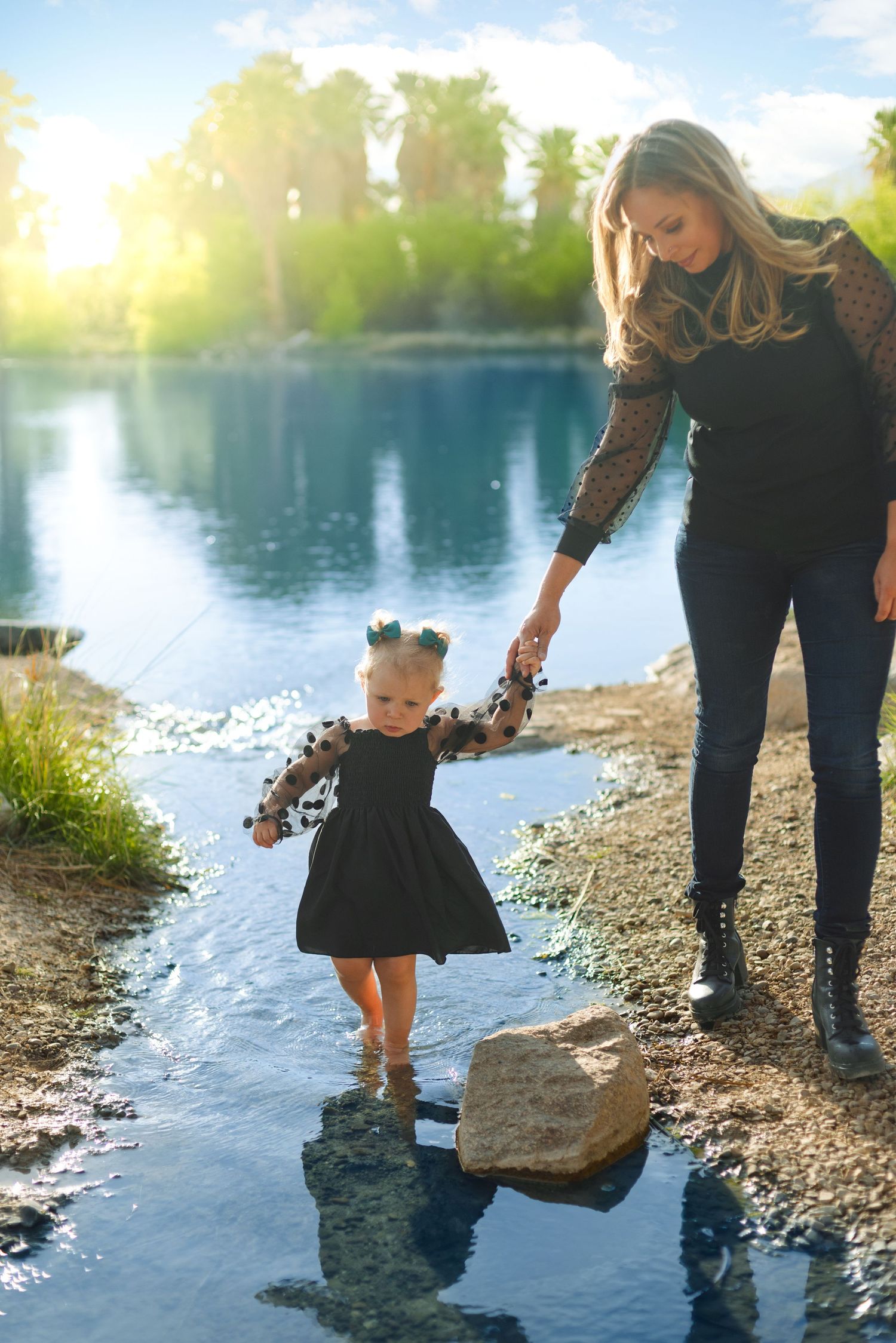 Parent and child holding hands by tranquil lake at sunset.