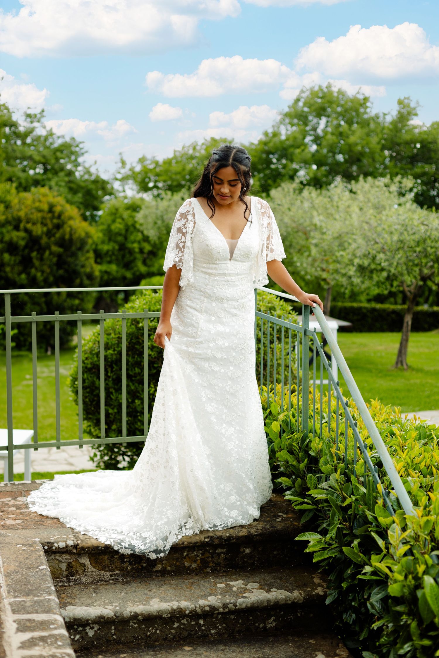 A wedding dress spreads elegantly across stone steps in a garden setting.