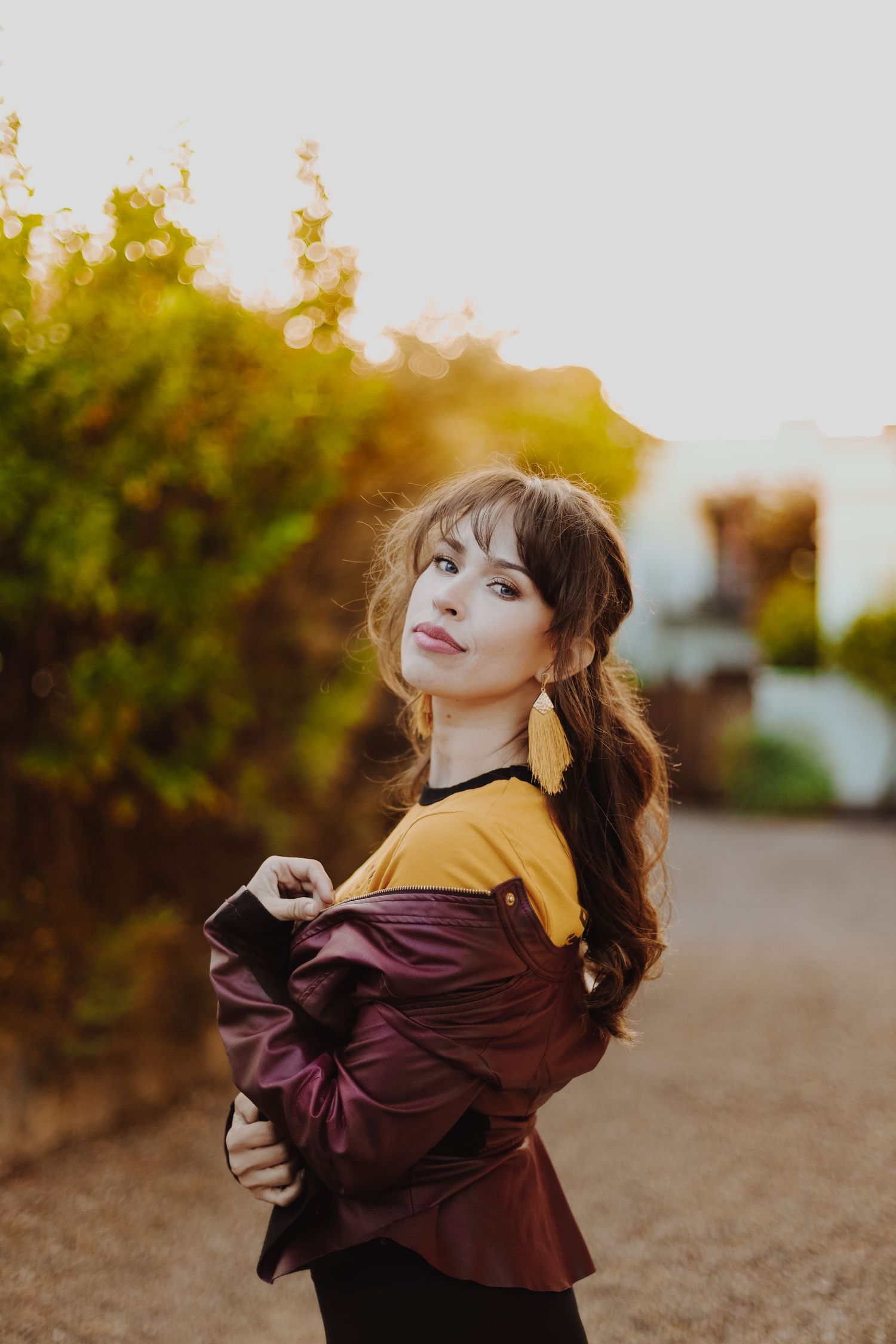 Woman in yellow and burgundy top poses outdoors at sunset.