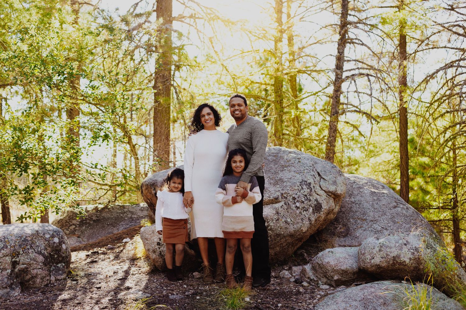 A family takes outdoor photos on a large fallen tree trunk in a forest setting.