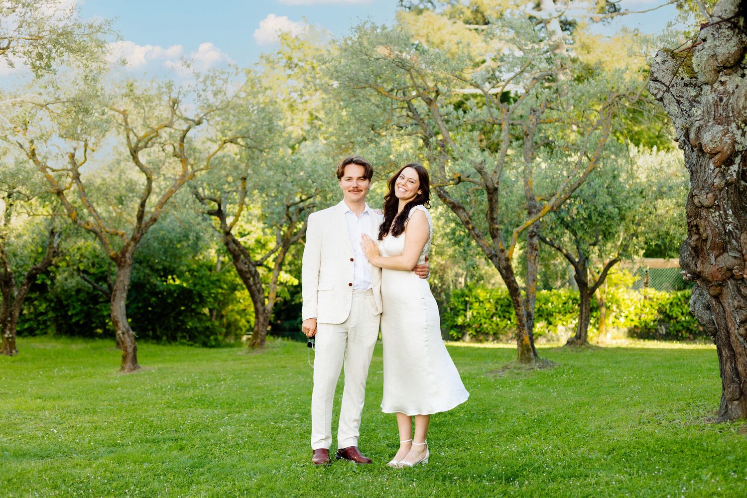 Couple walks through a sunlit orchard during their wedding photoshoot.