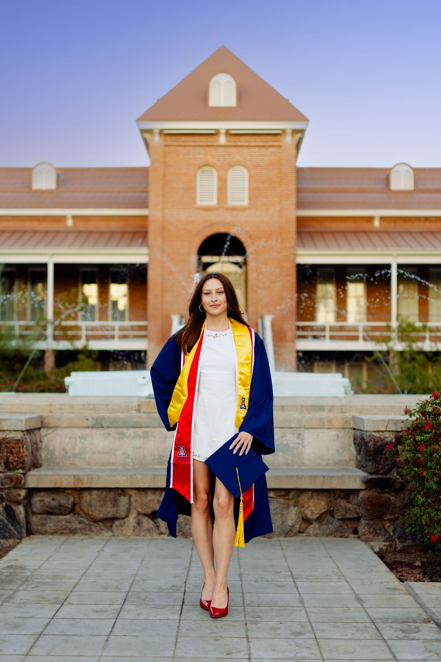 Graduation photos in front of a brick building wearing academic regalia with blue and gold stoles.