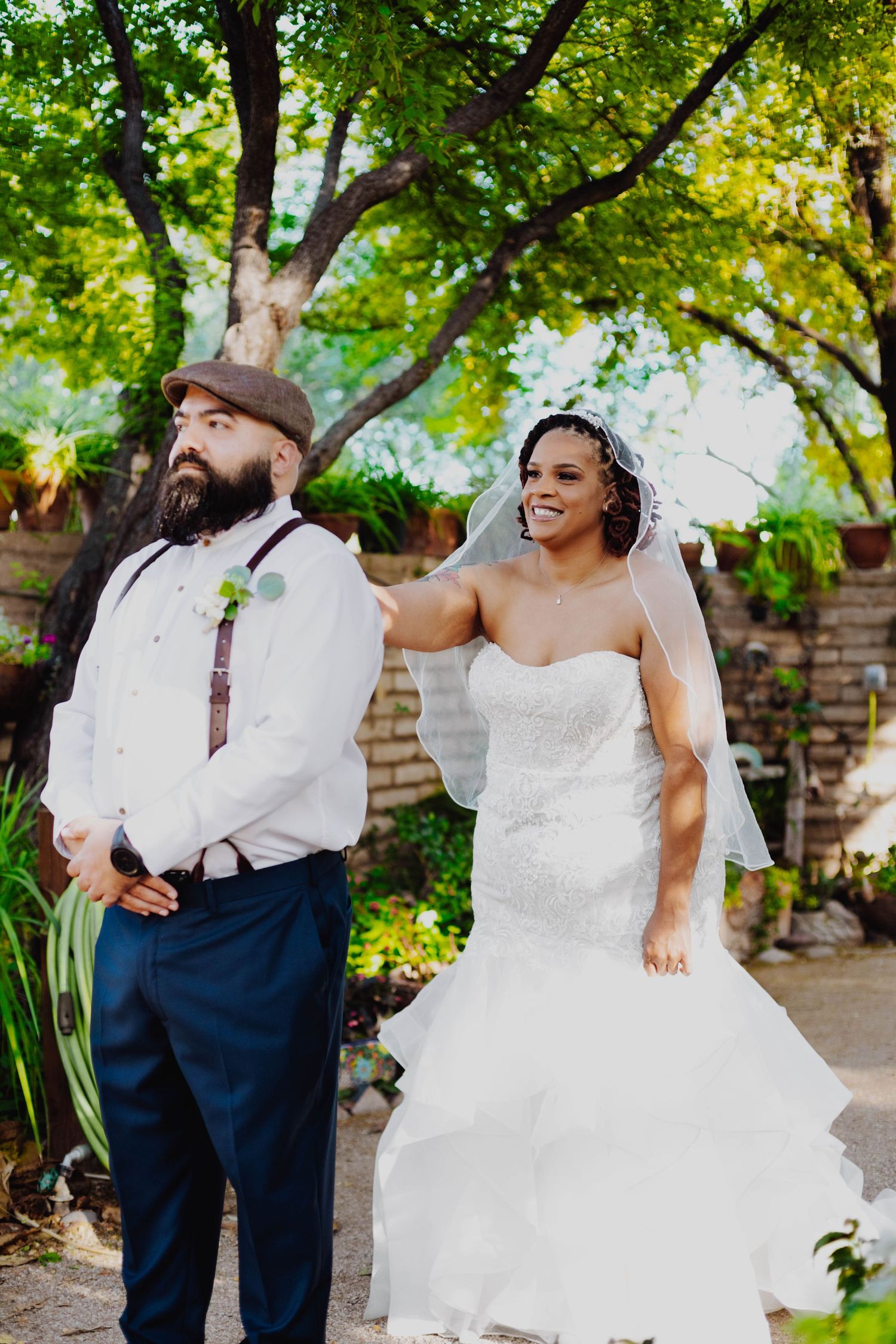 Garden wedding portrait with lush green trees and brick wall backdrop.