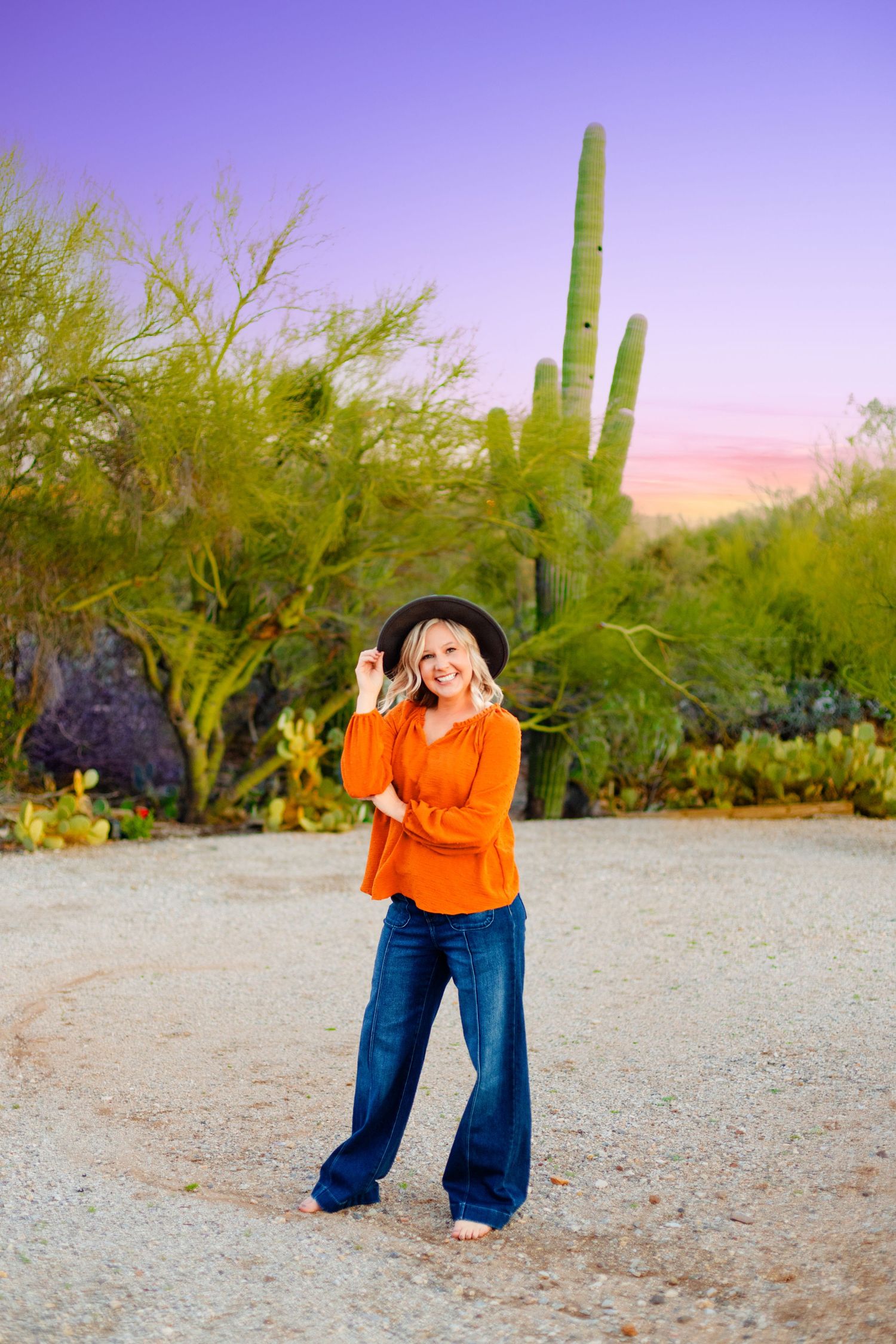 Fashion photoshoot in a desert landscape with orange top and wide-leg jeans at sunset.