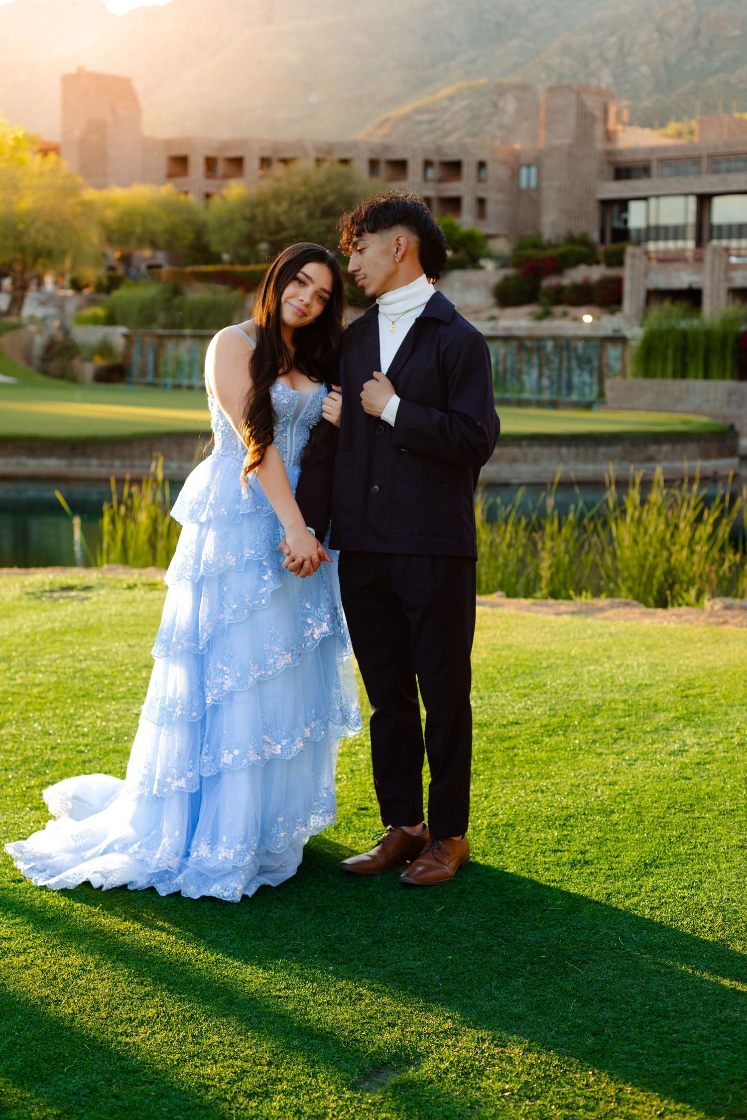 Romantic couple portraits on green lawn at sunset with building in background.