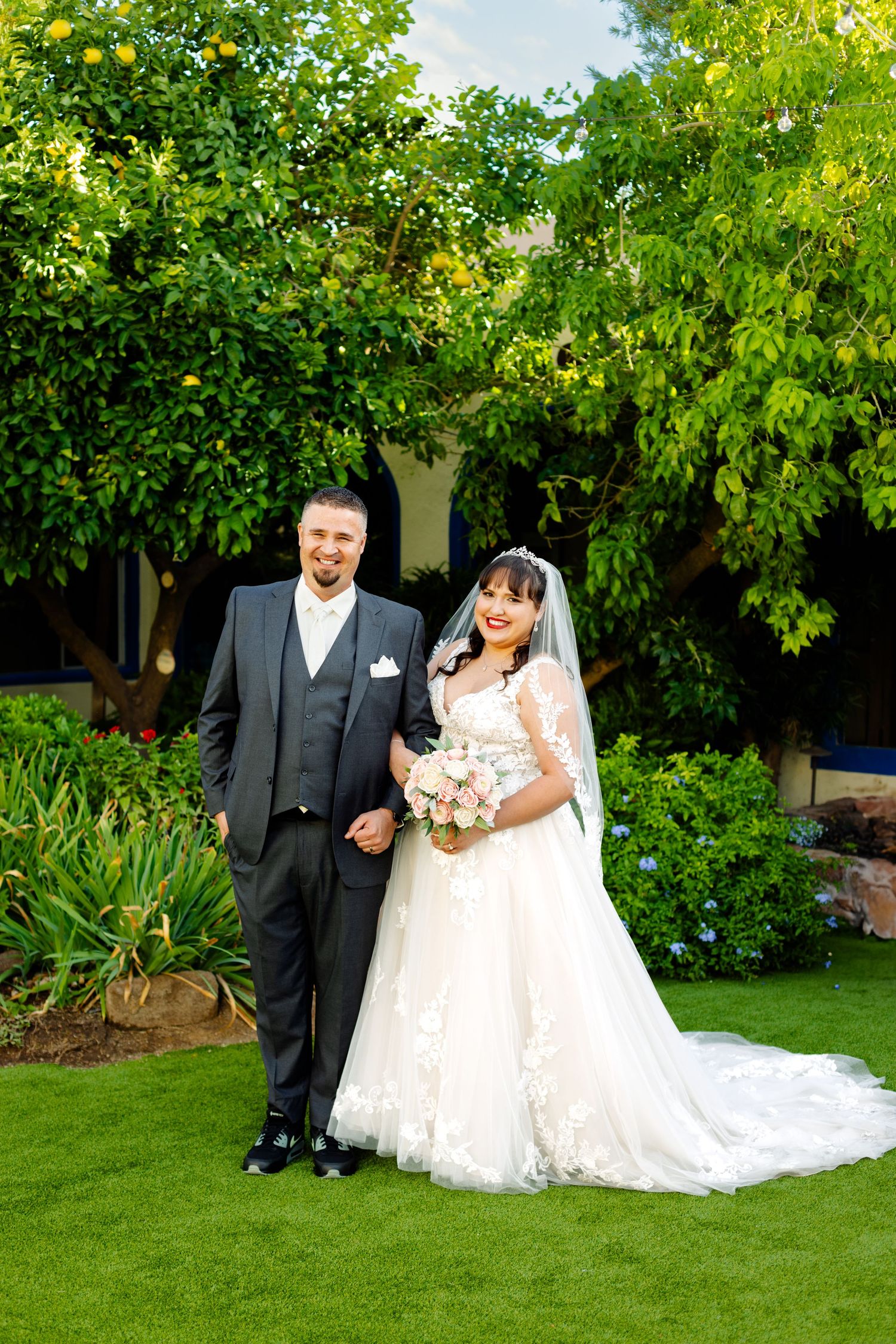 Wedding portrait of couple standing on manicured garden lawn surrounded by greenery.
