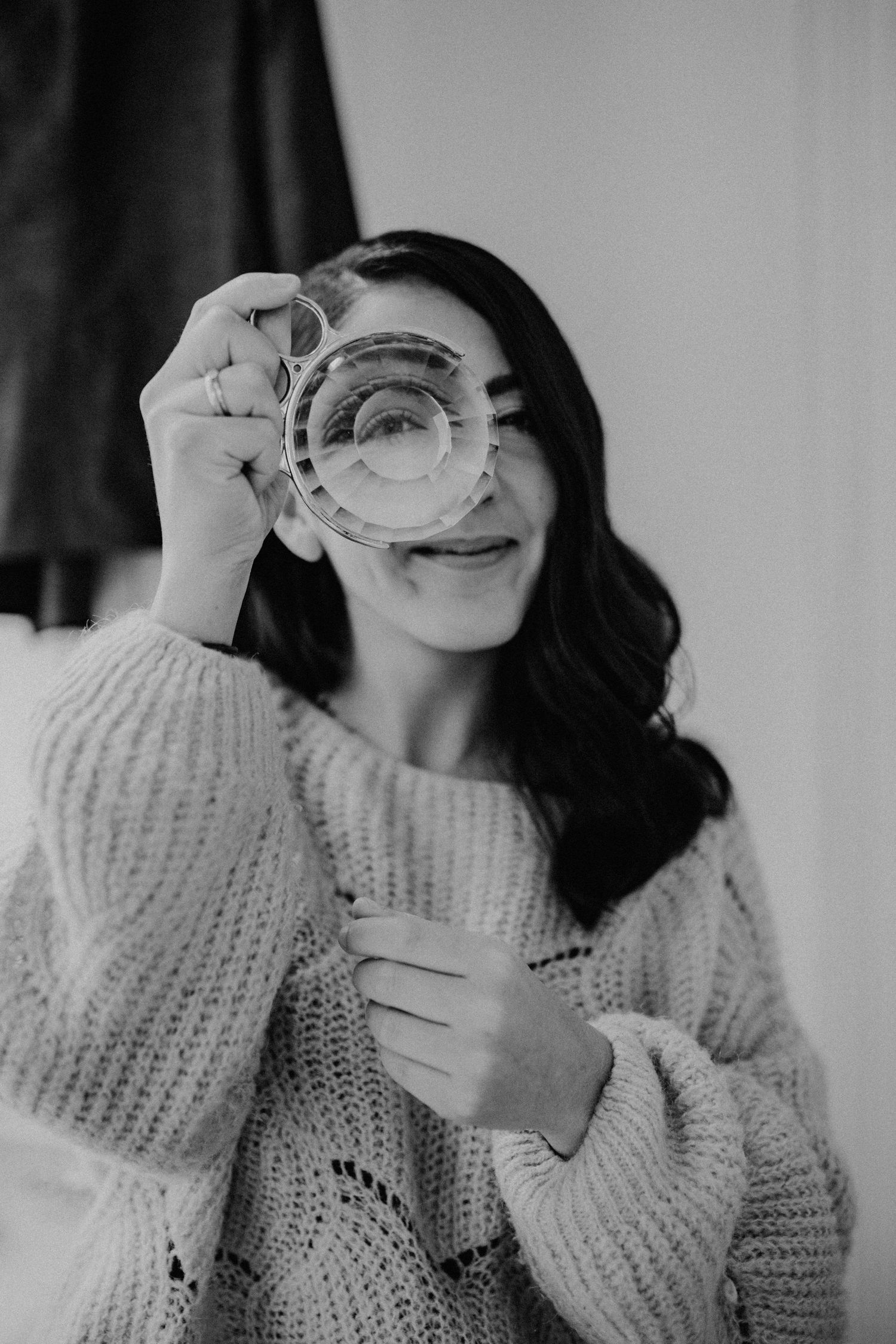 Black and white portrait of someone looking through a crystal glass with a playful expression.