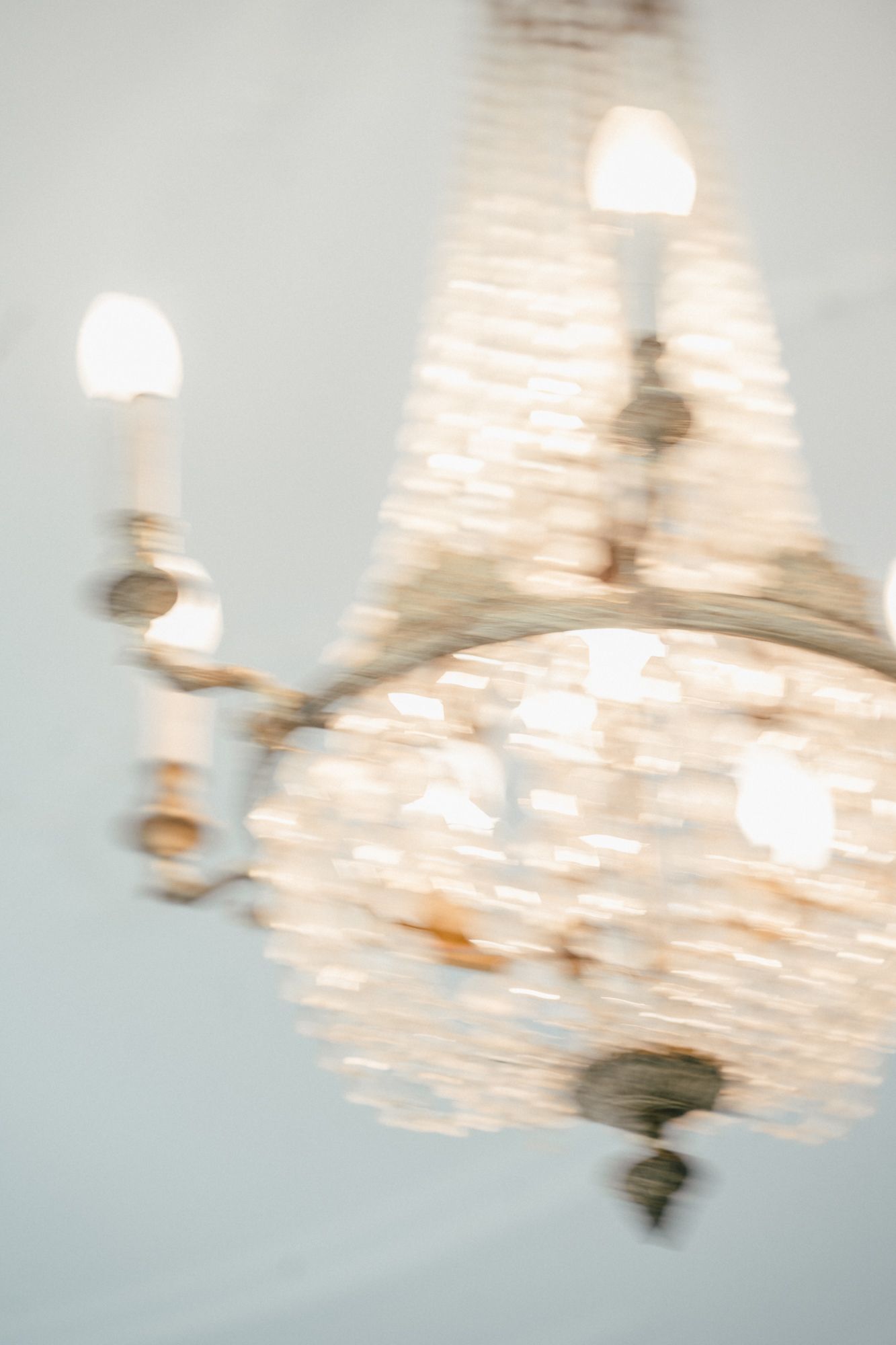 Motion-blurred crystal chandelier creating an ethereal golden glow against a pale background.