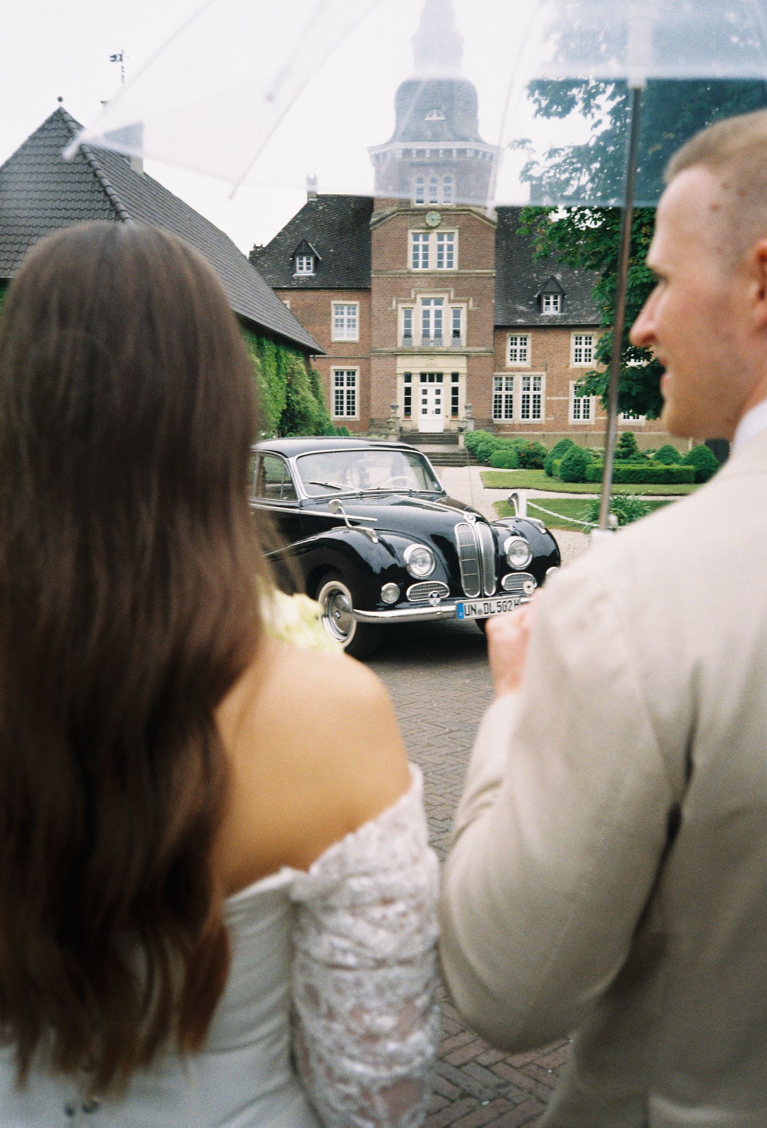 Classic vintage car parked outside a grand brick manor house.