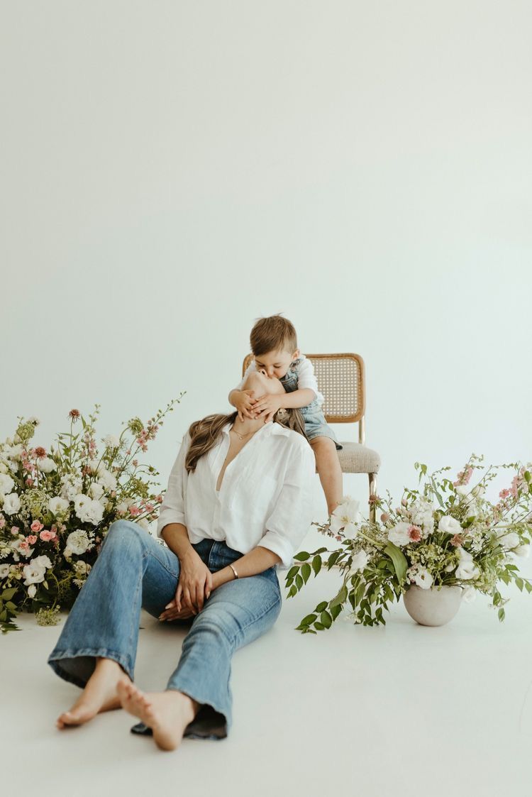 Minimalist portrait with white flowers and greenery arrangements on a bright backdrop with someone holding a small kitten.