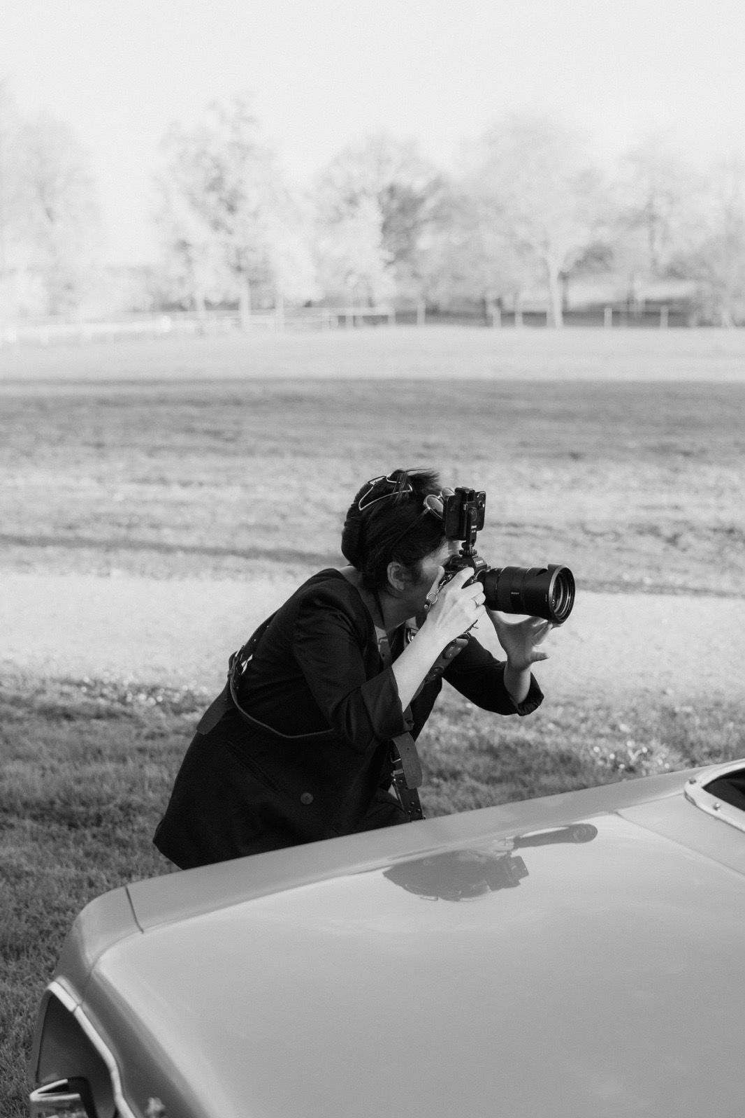 Photographer leaning over car hood taking pictures in black and white landscape.
