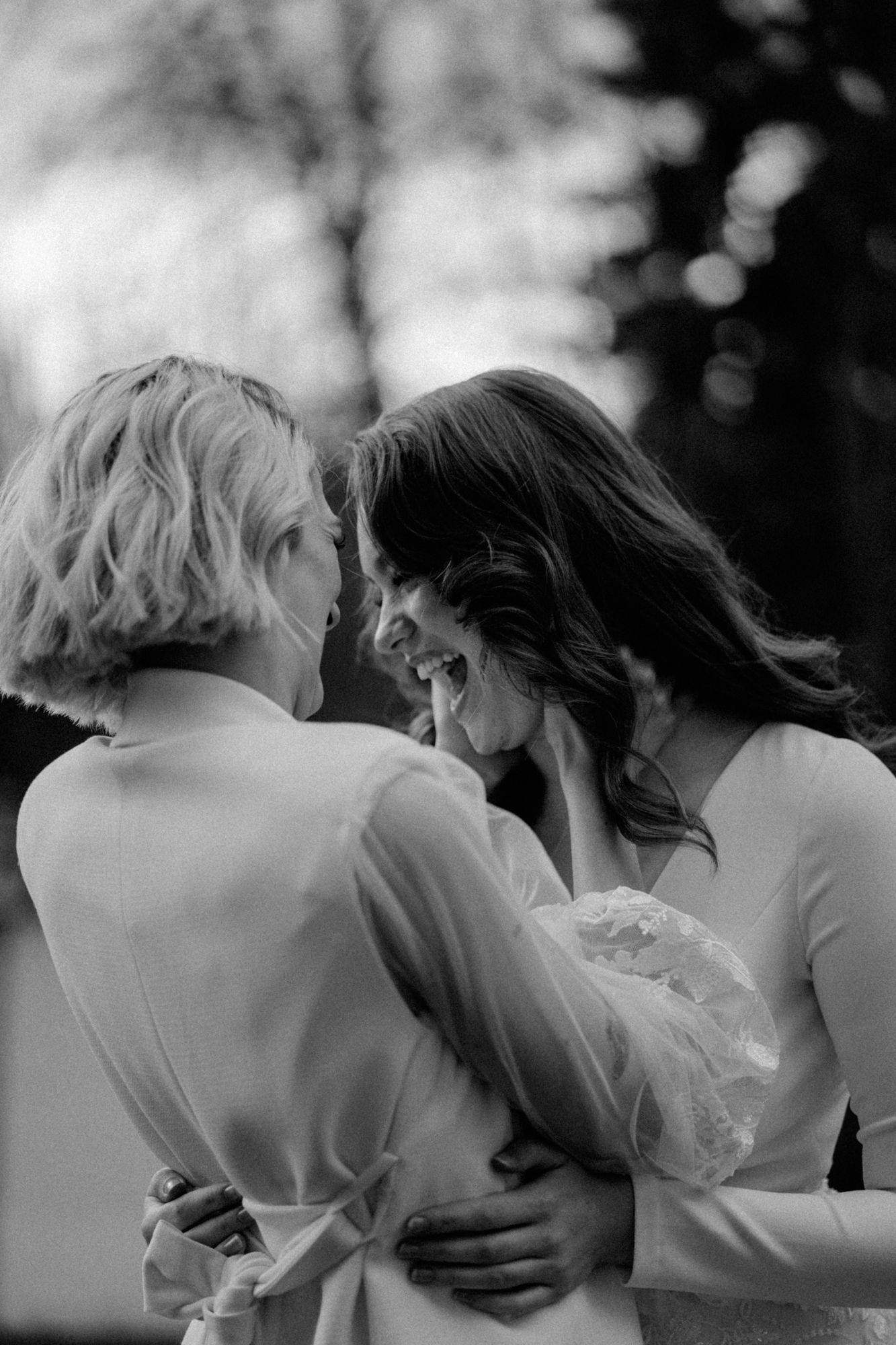Black and white photograph showing two people embracing in an intimate moment outdoors.