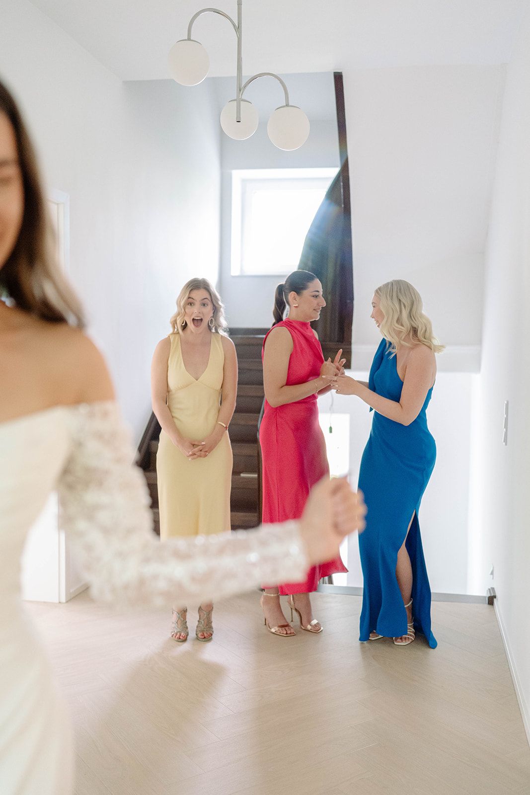 Wedding preparation scene with women in colorful dresses standing in a bright hallway.