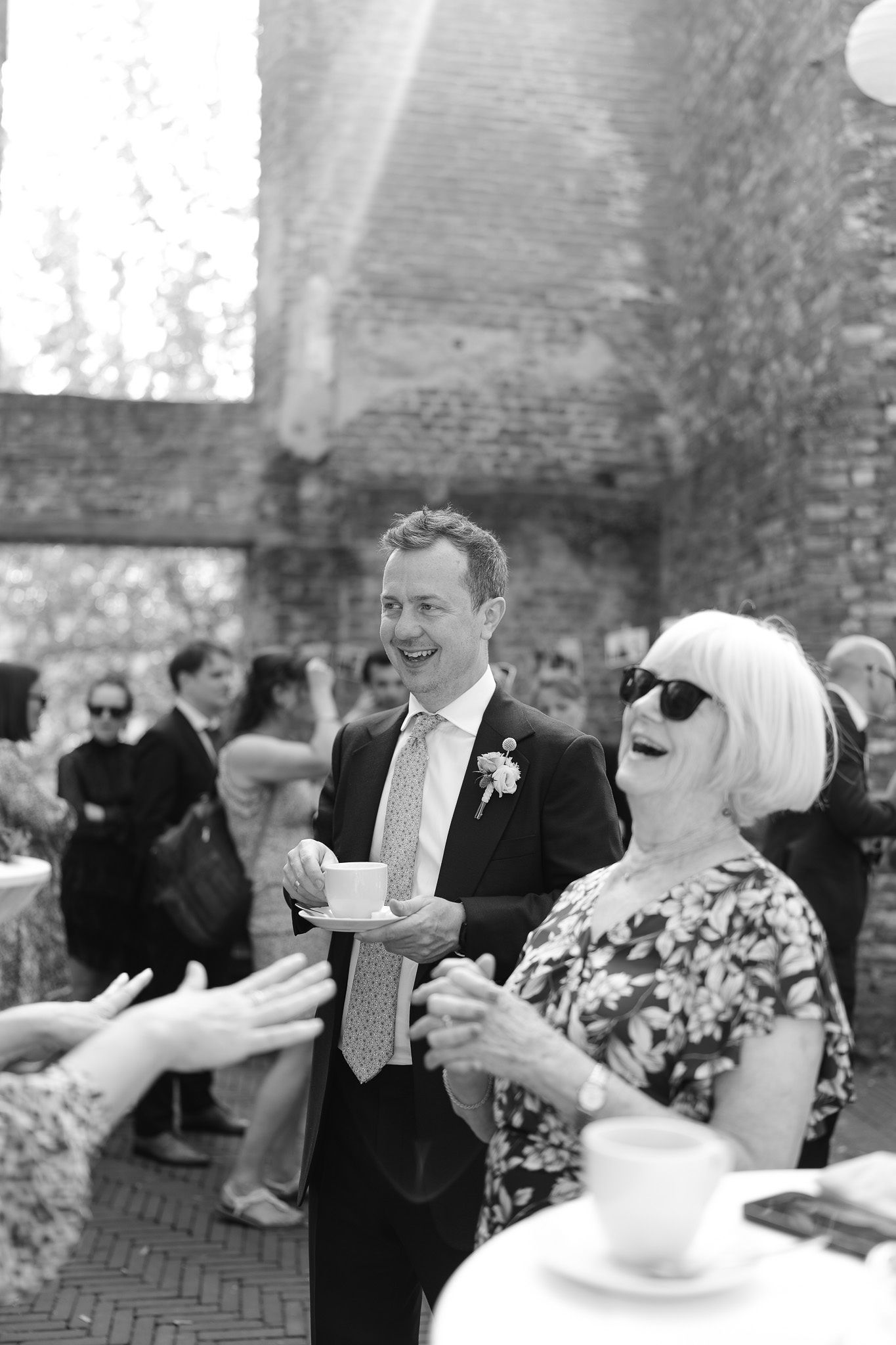 Wedding guests mingling outdoors near a brick building during a daytime reception.